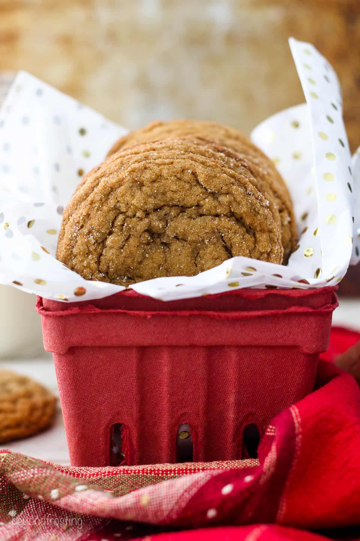 side view of a red container lined with tissue paper and filled with molasses cookies