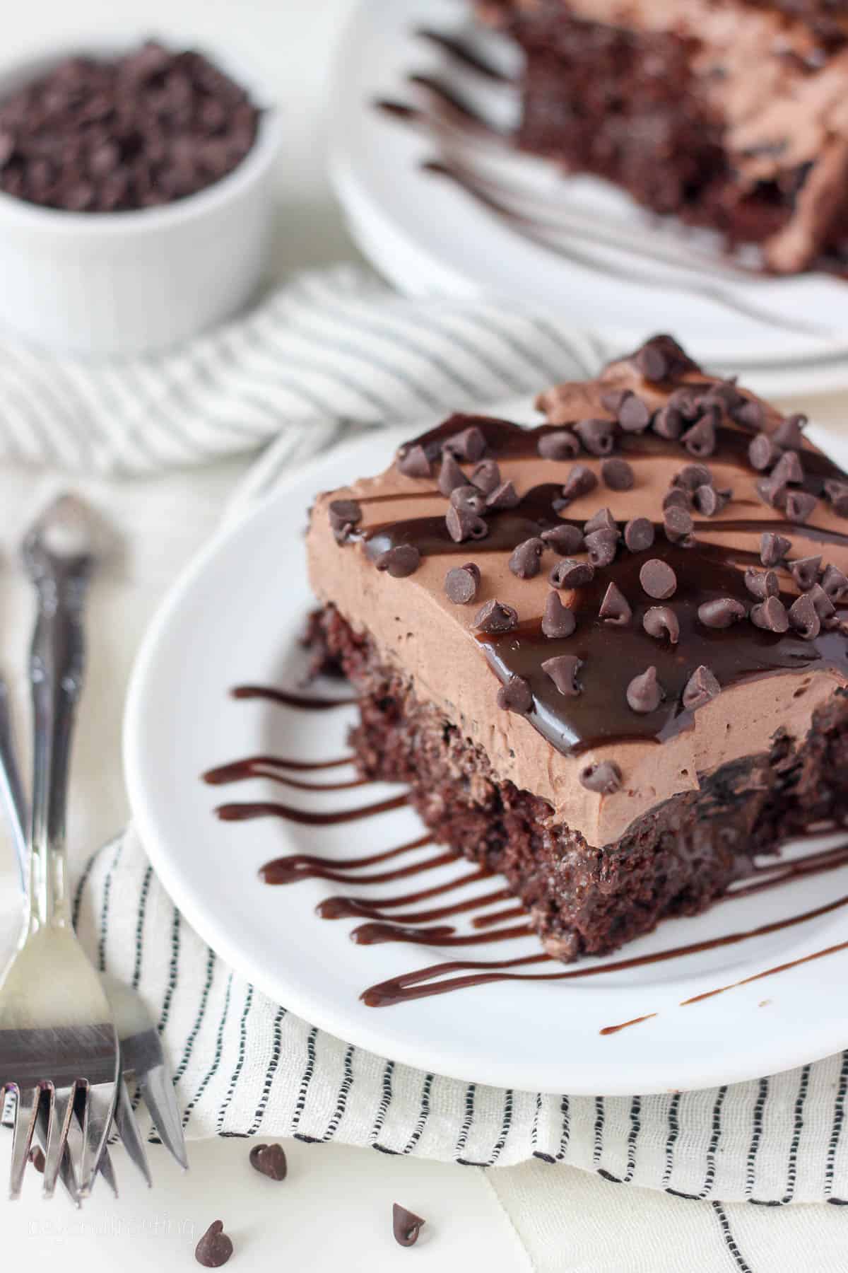 overhead of a square slice of chocolate poke cake on a white plate next to two forks