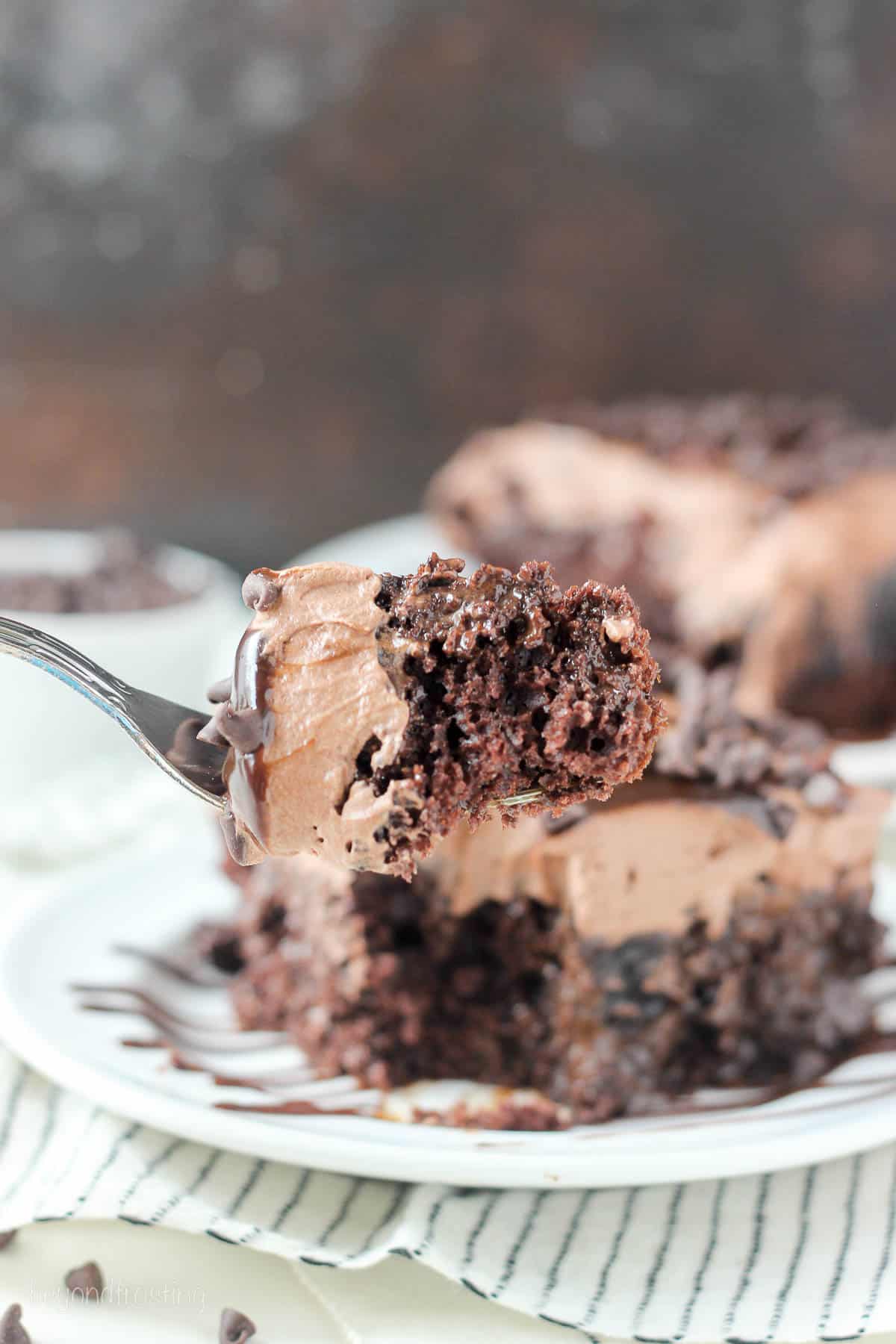 a forkful of chocolate poke cake held in front of a plate with a slice of cake