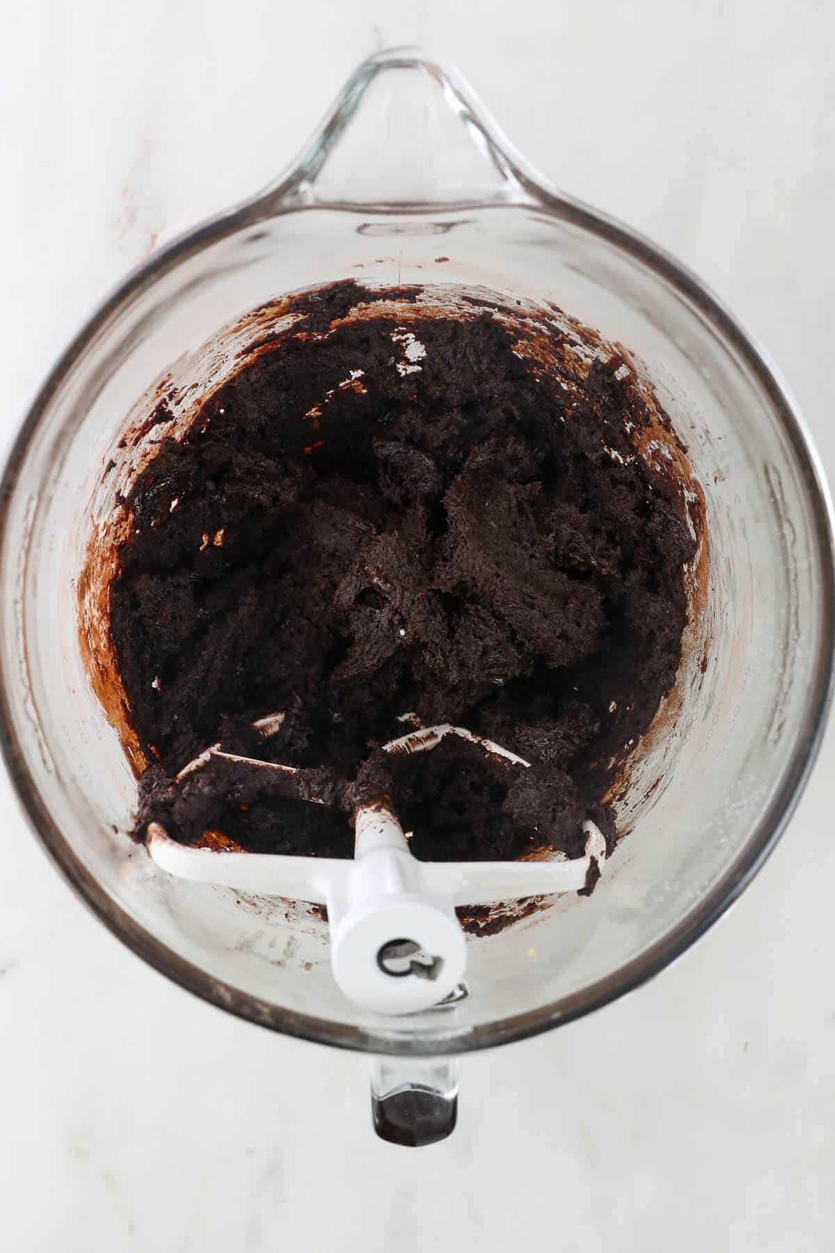 Chocolate cookie dough in a glass bowl with a stand mixer attachment.