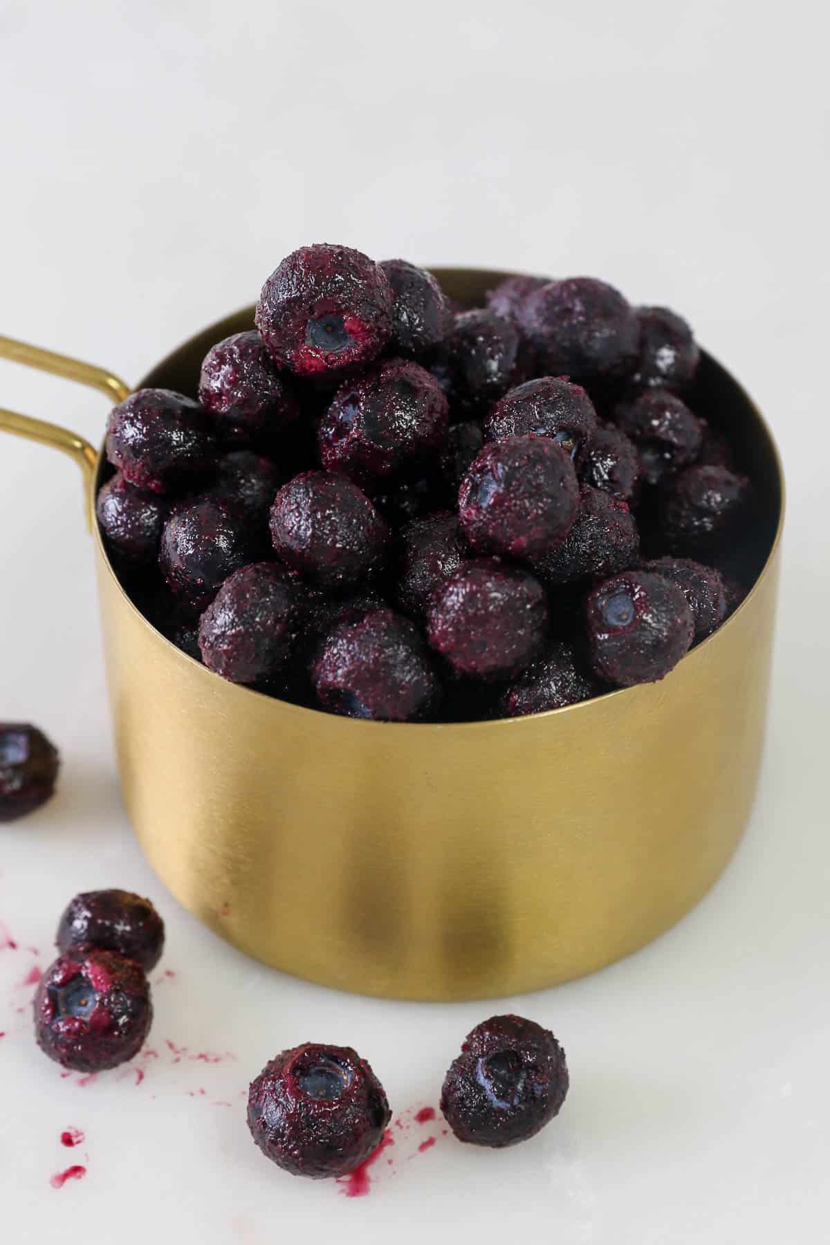 a gold measuring cup filled with frozen blueberries
