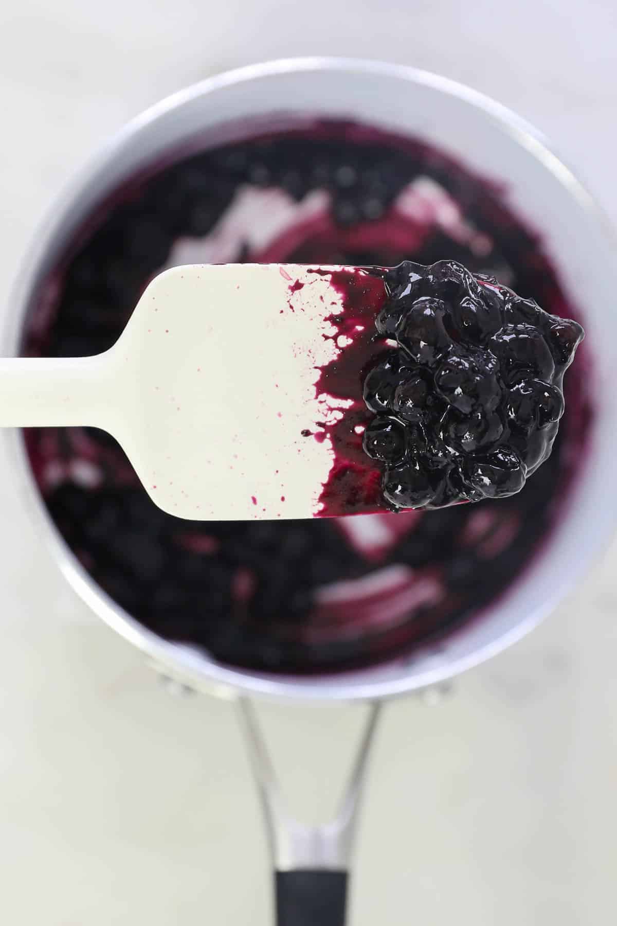 A white spatula holding a spoonful of blueberry sauce