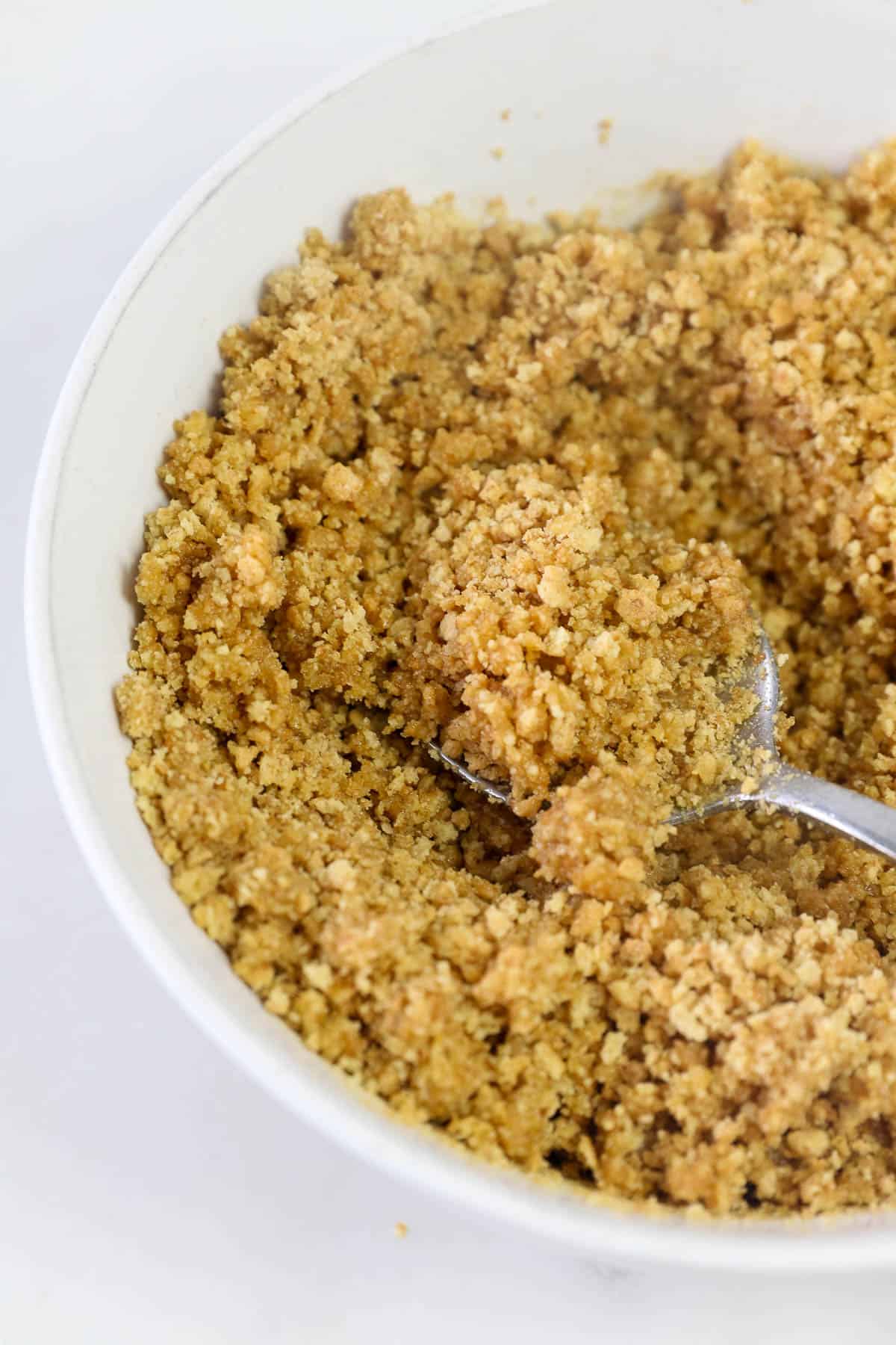 graham cracker crumbs with butter mixed in a bowl with spoon