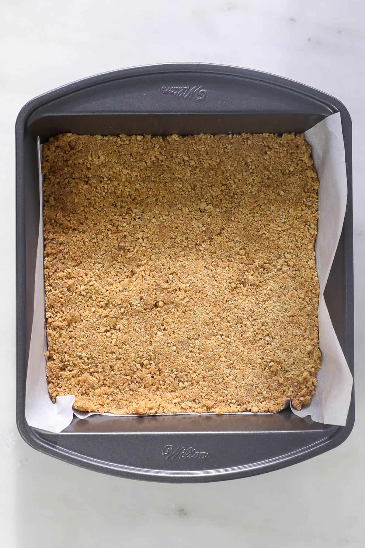 overhead view of a baking pan with parchment paper and a graham cracker crust