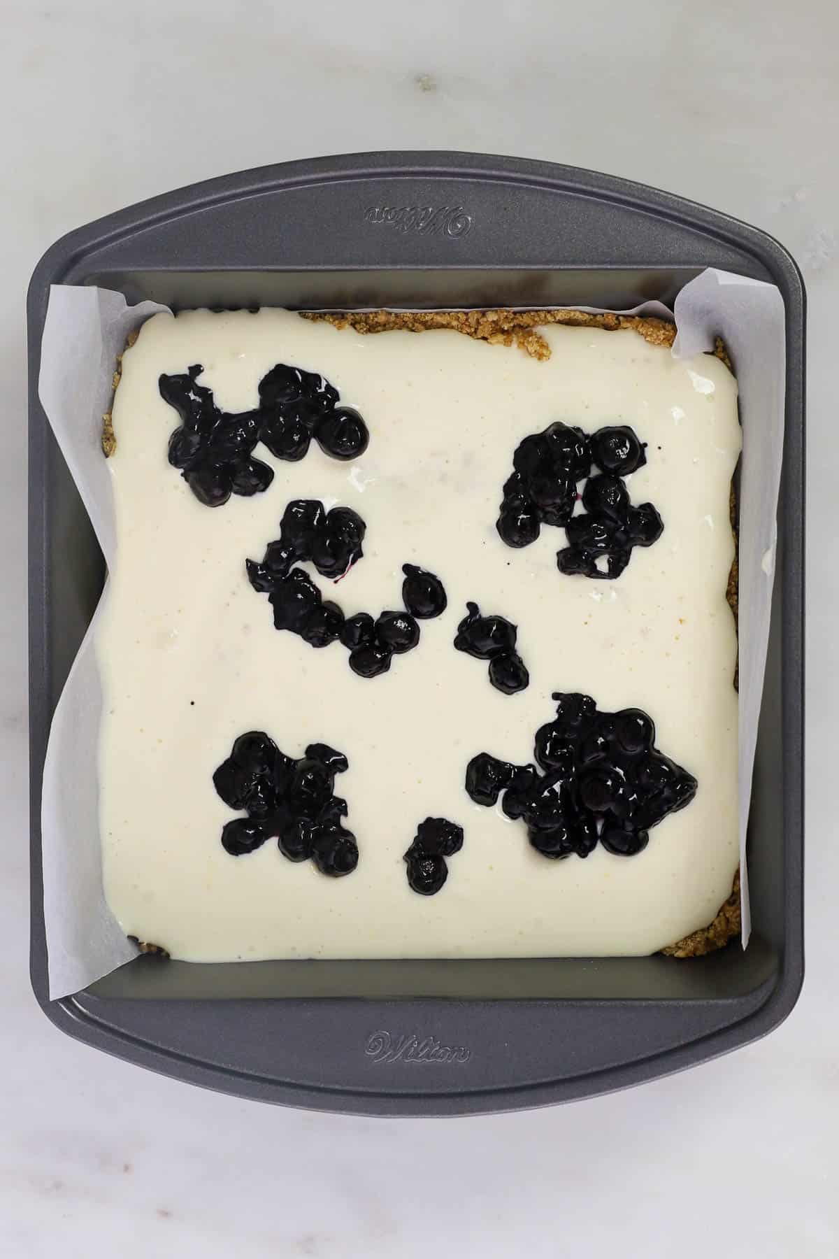 overhead view of a baking pan with cheesecake batter with dollops of blueberry sauce
