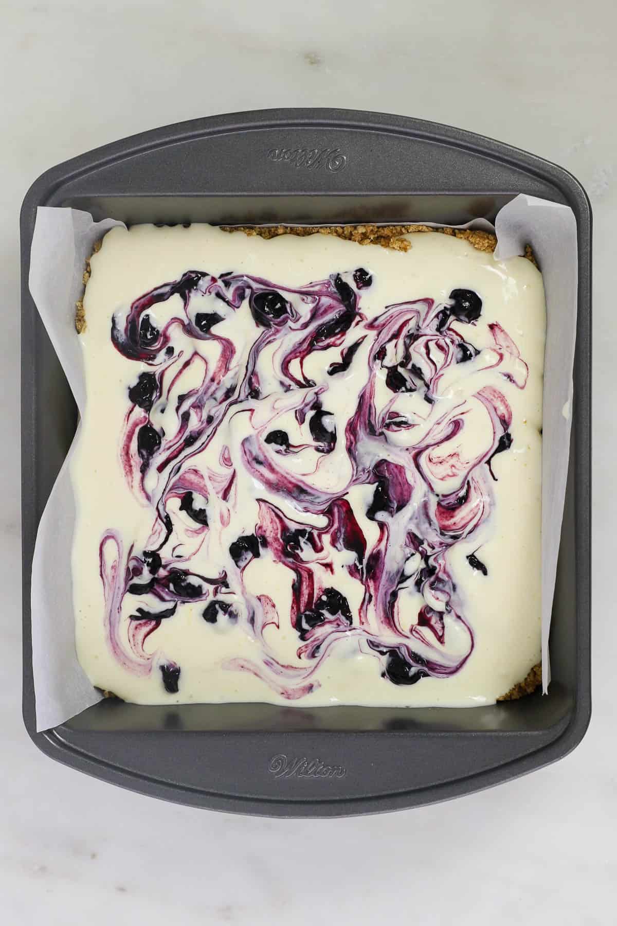 overhead view of a baking pan with cheesecake batter swirl with blueberries
