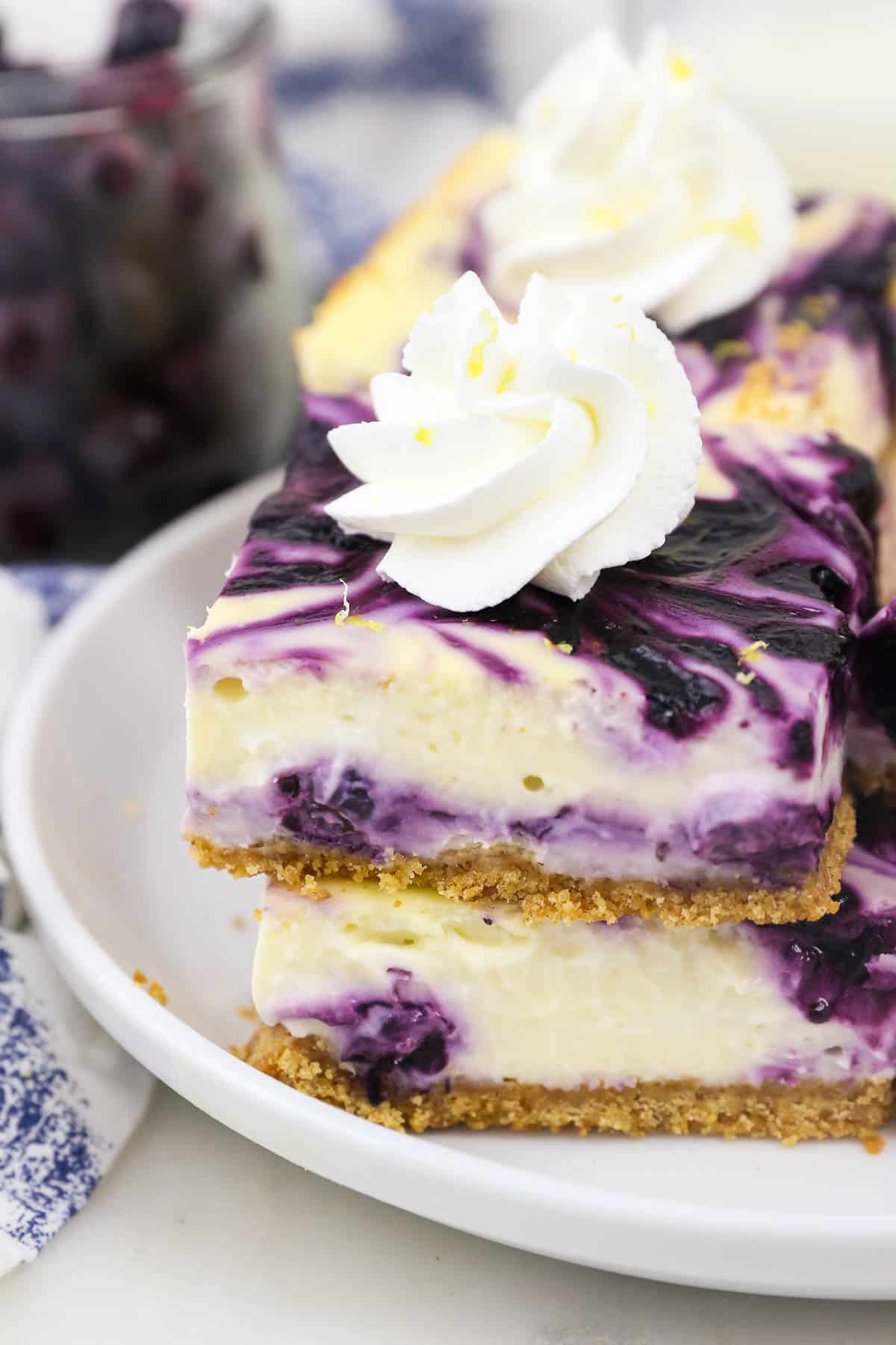 two blueberry cheesecake bars, stacked with whipped cream on tpo