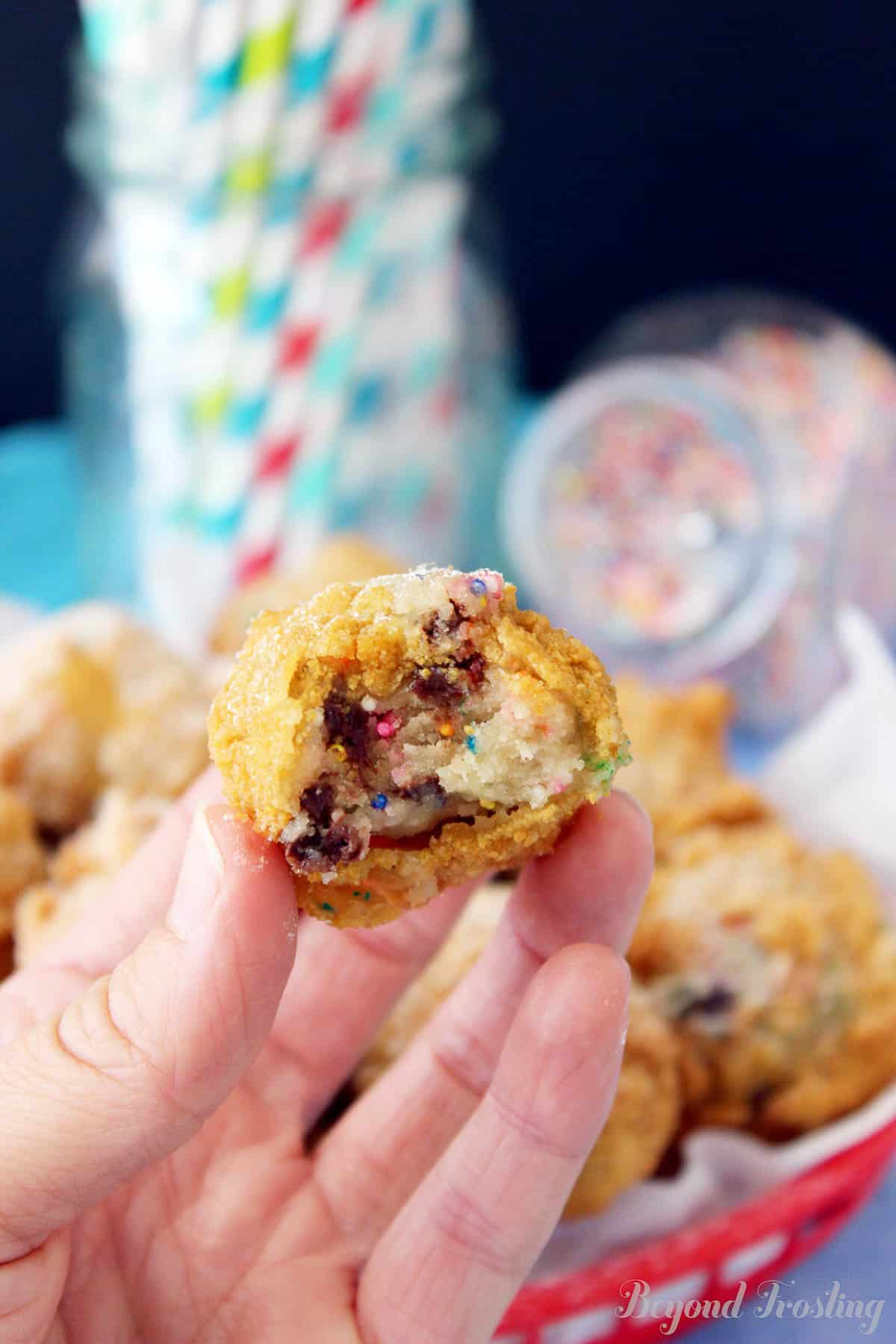 A hand holding up a piece of deep friend cookie dough with a bite missing