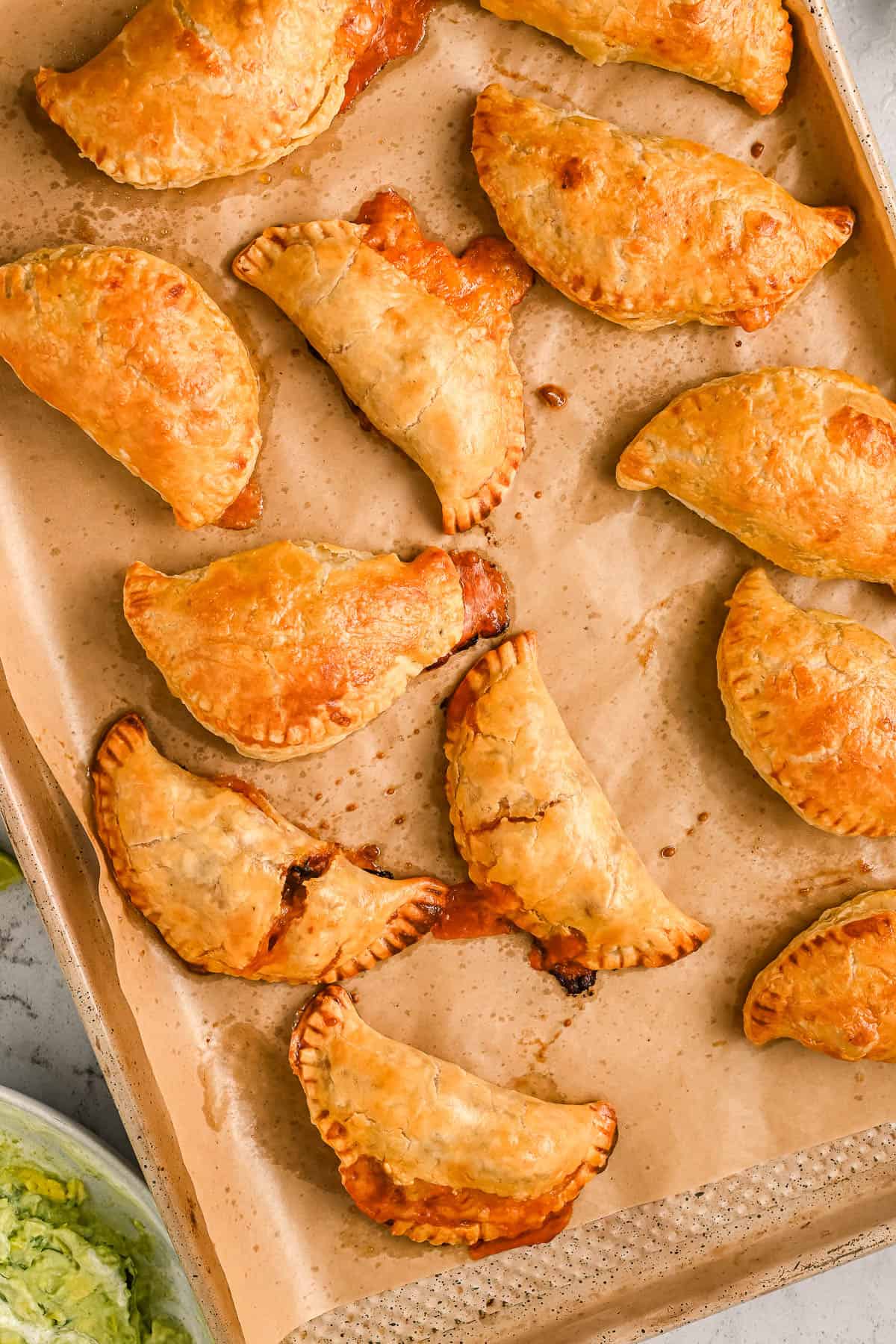 Crispy baked chicken empanadas on a parchment-lined baking sheet.
