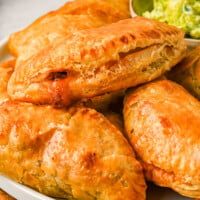 Close up of chicken empanadas stacked on a plate next to a bowl of avocado crema.