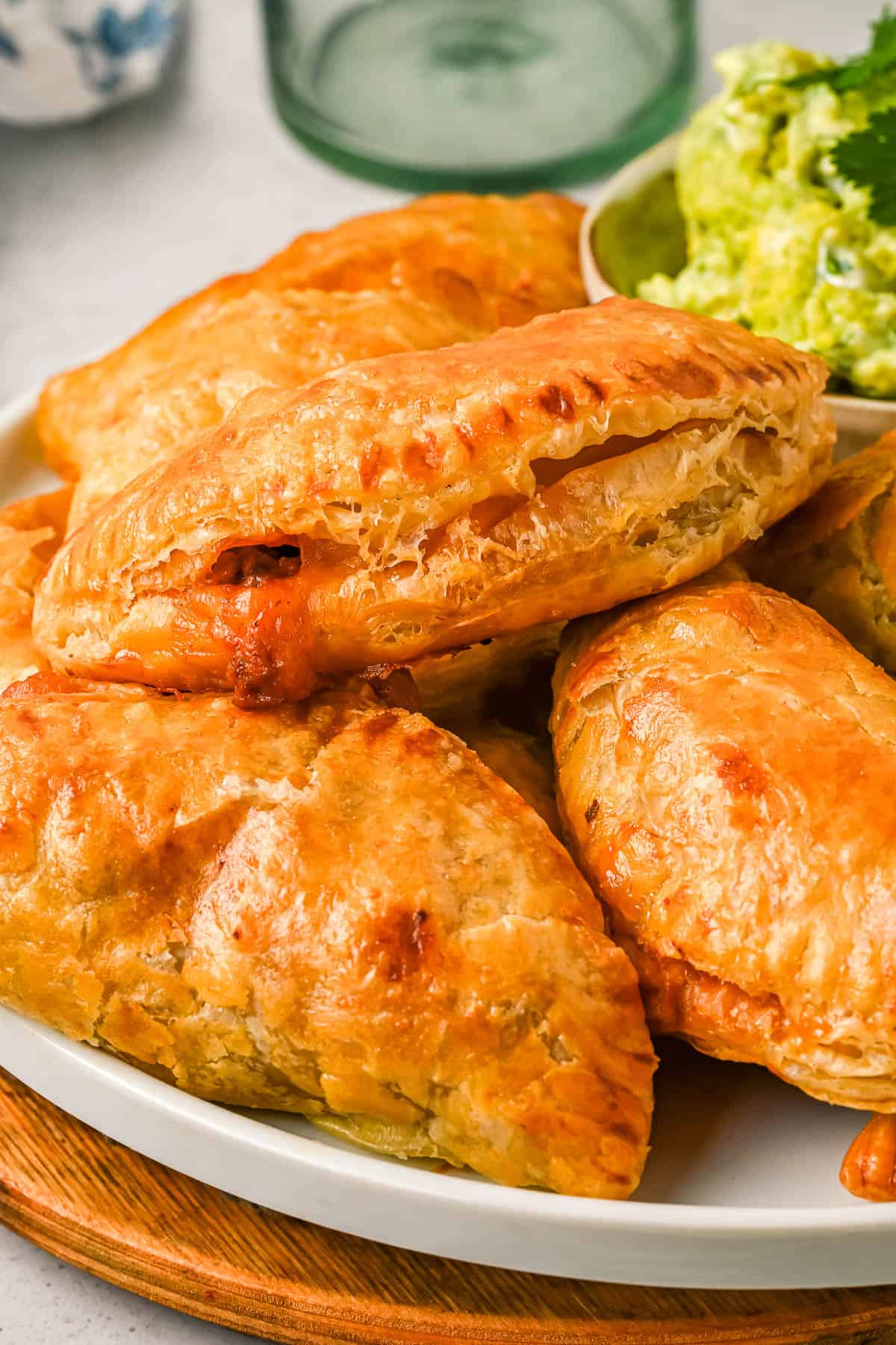 Close up of chicken empanadas stacked on a plate next to a bowl of avocado crema.