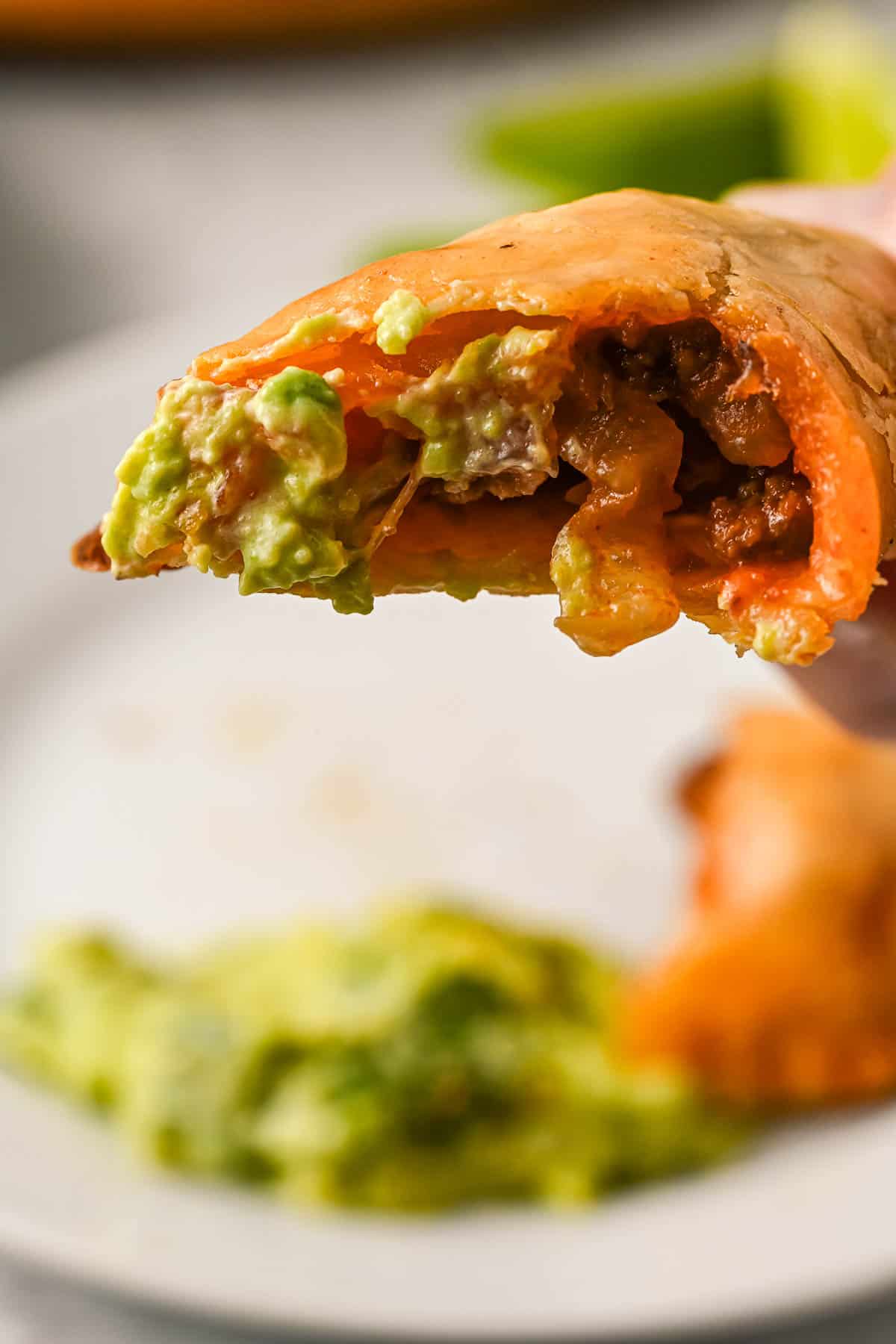 Close up of a chicken empanada with a bite missing, with a plate in the background.