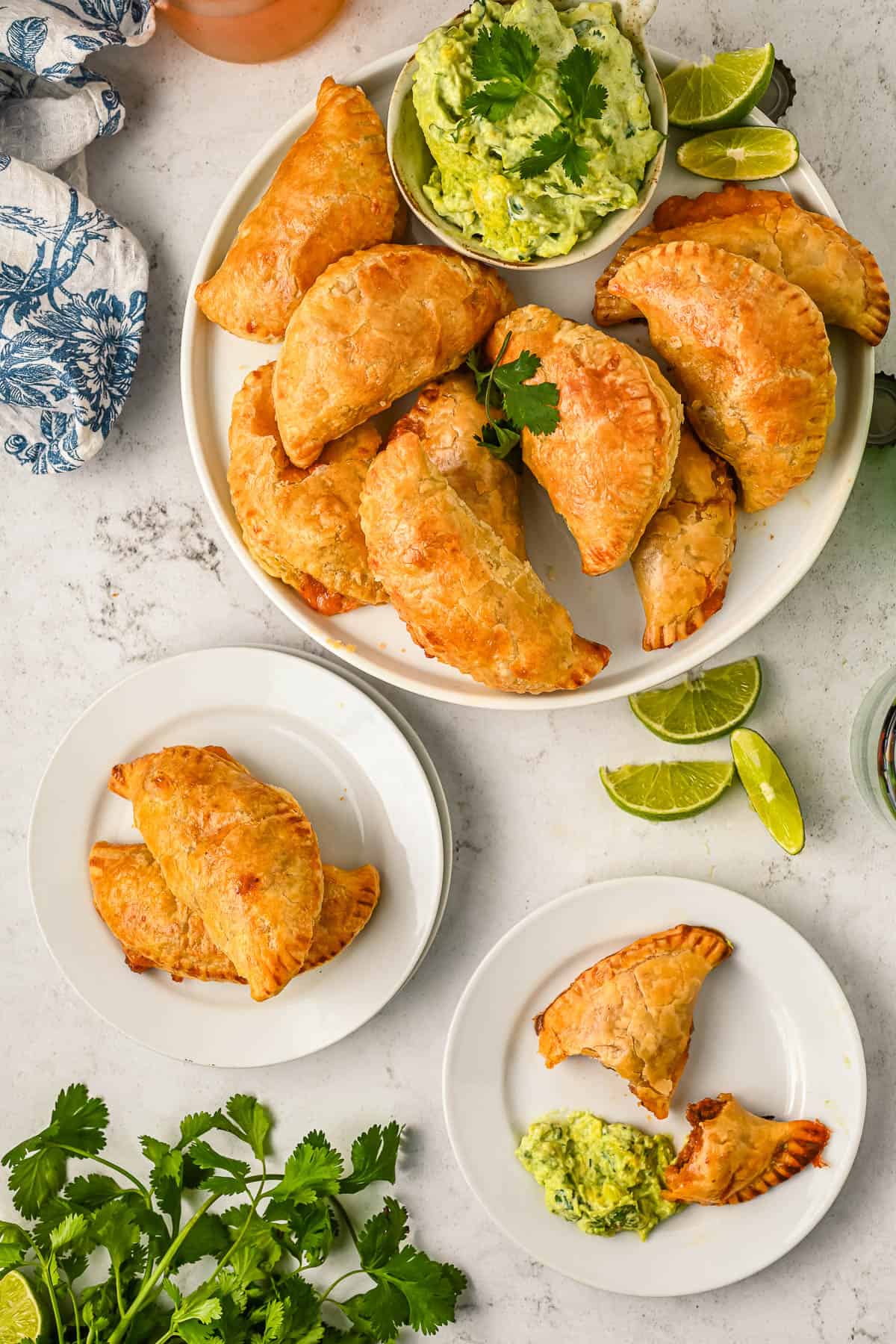 Overhead view of a platter of chicken empanadas next to two smaller plates with empanadas and avocado crema.