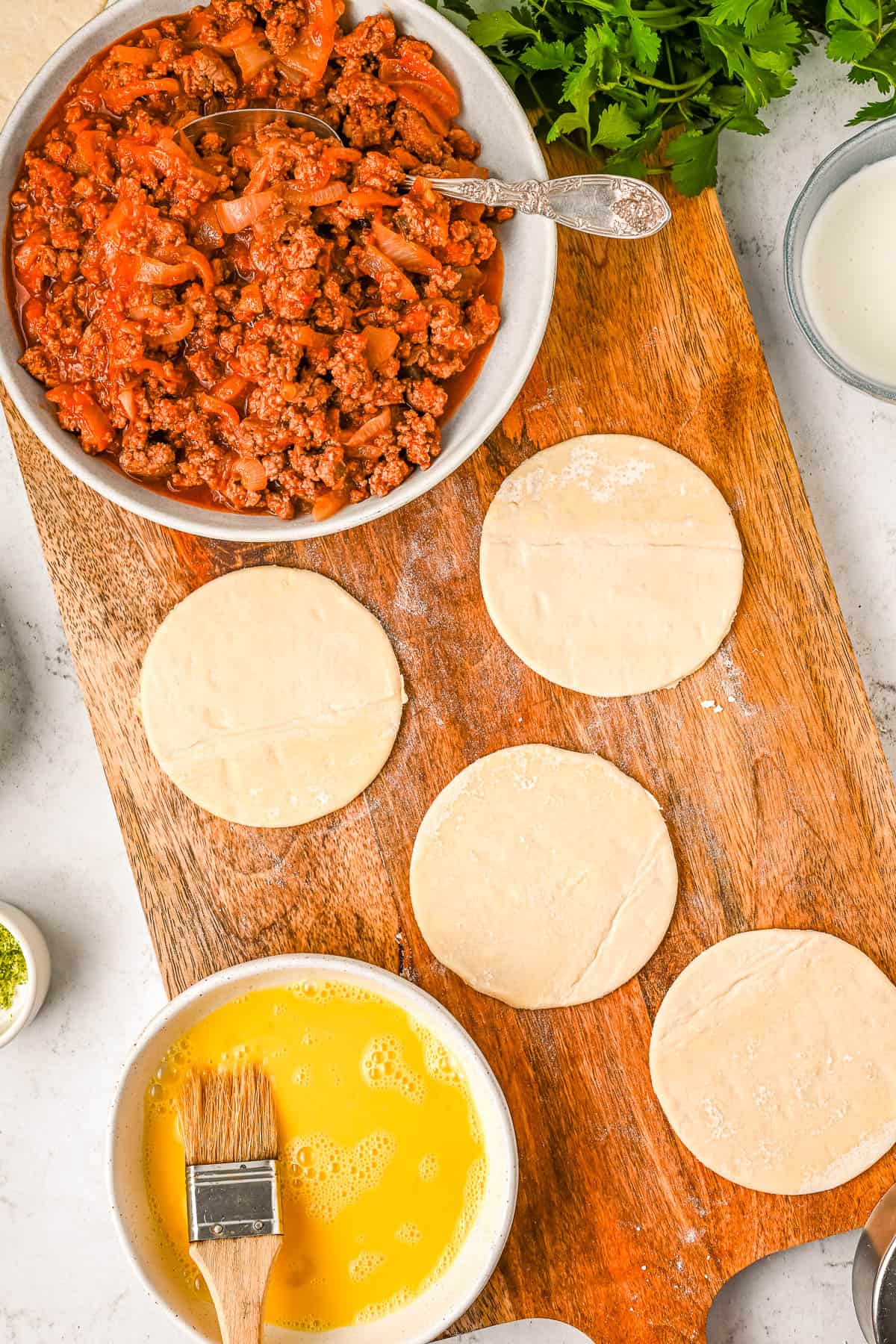Empanada dough rounds laid out on a wooden cutting board, ready to be topped with chicken empanada filling and cheese.