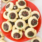 A red plate filled with chocolate thumbprint cookies decorated with sprinkles.