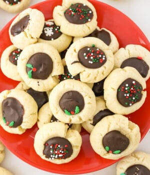 A red plate filled with chocolate thumbprint cookies decorated with sprinkles.
