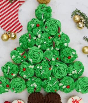 A completed Christmas tree cake with a star on top and presents underneath it, all made out of cupcakes, frosting and sprinkles