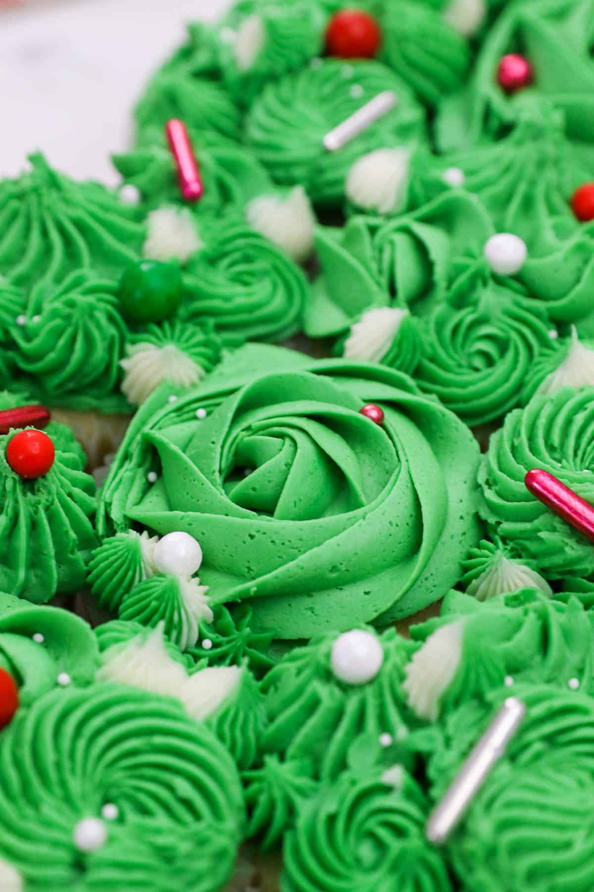 A close-up shot of cupcakes frosted with green buttercream designs and topped with sprinkles