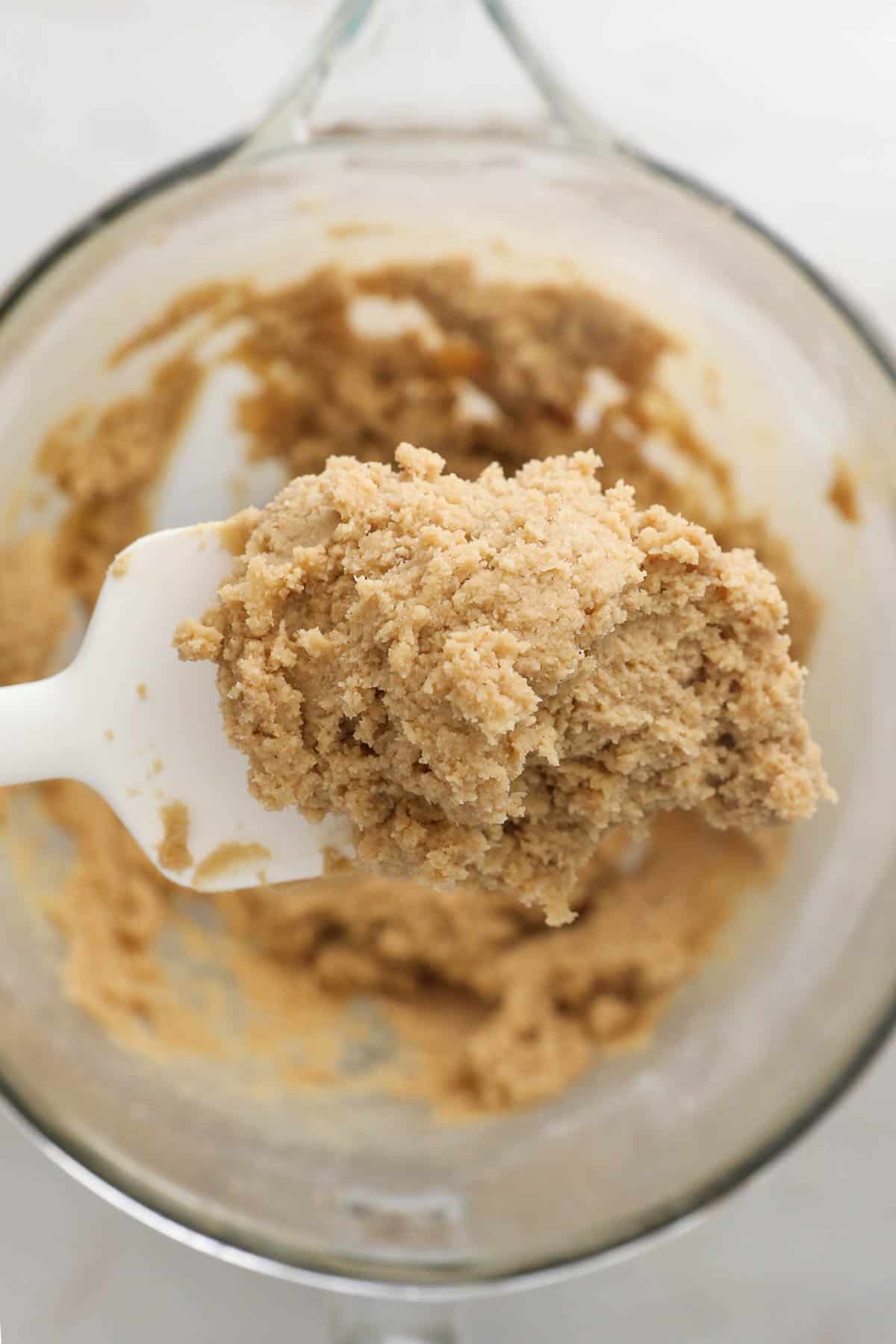 overhead of a bowl of cookie dough with a spatula held above.