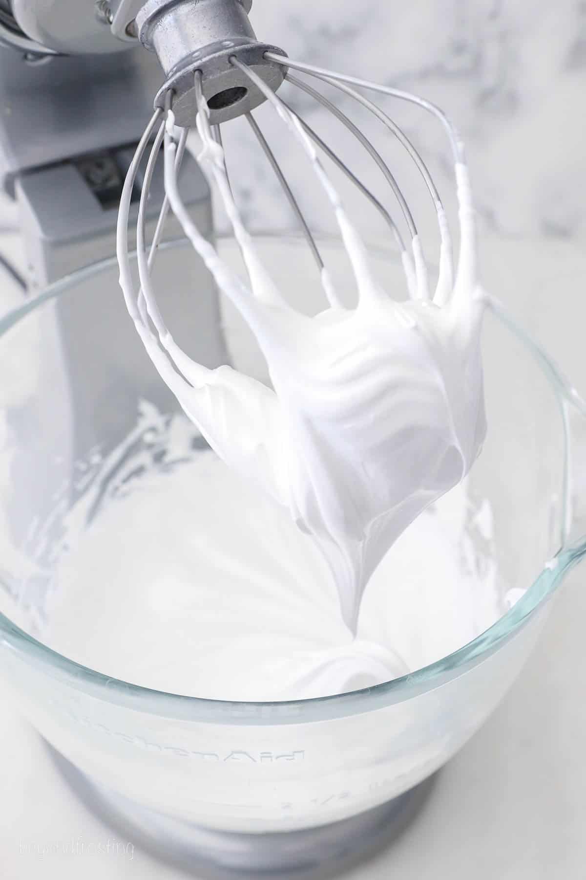 A mixing bowl with marshmallow frosting beneath the whisk attachment of a stand mixer.