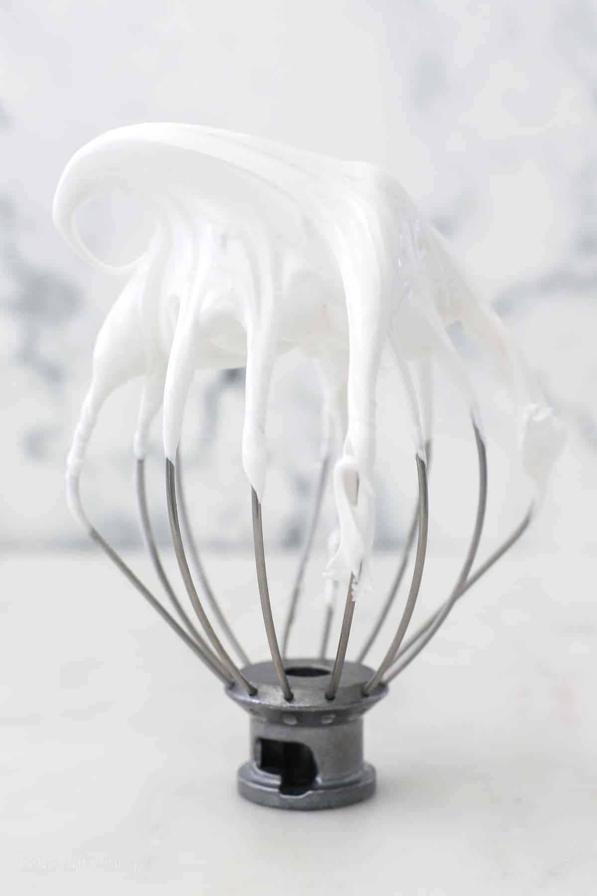 The whisk attachment of a stand mixer propped upright, topped with marshmallow frosting.