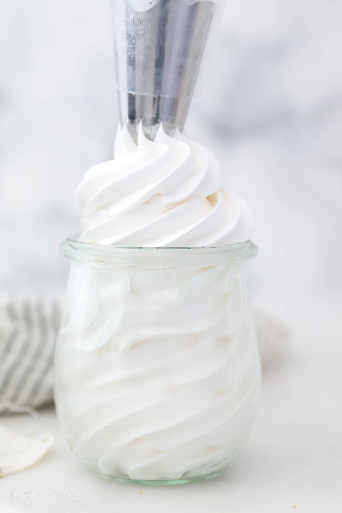 A piping tip piping marshmallow frosting into a glass jar.