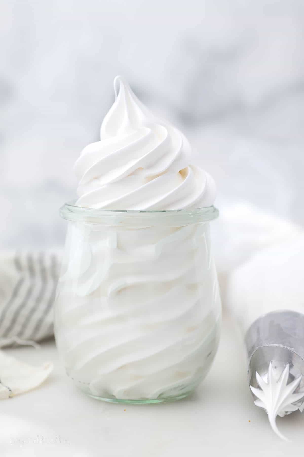 Marshmallow frosting piped into a glass jar next to a piping bag.