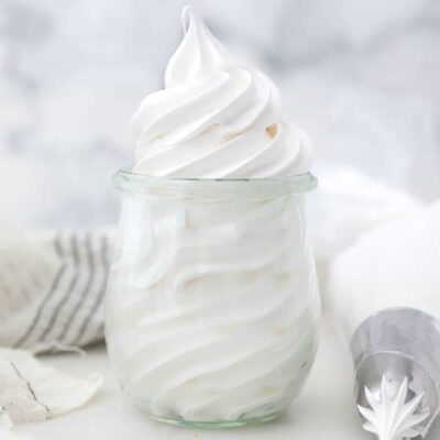Marshmallow frosting piped into a glass jar next to a piping bag.