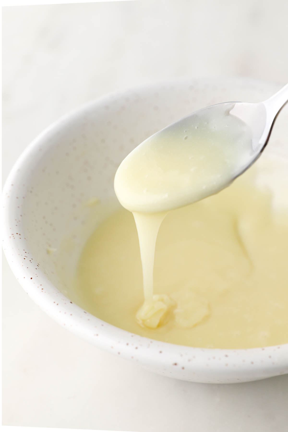 white chocolate ganache being drizzled off of a spoon over a bowl
