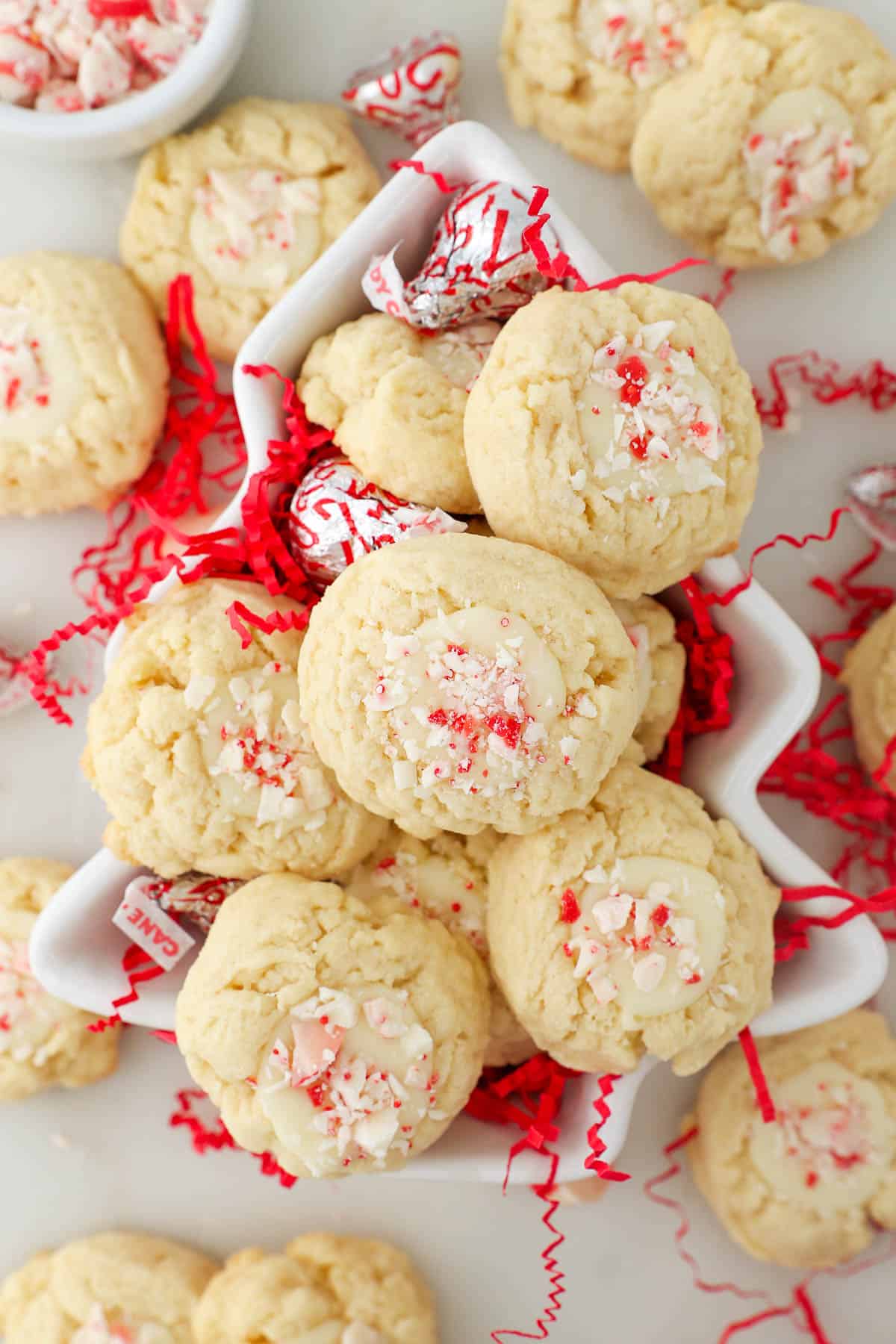 overhead of a white bowl shaped like a Christmas tree filled with and surrounded by peppermint cream thumbprint cookies.