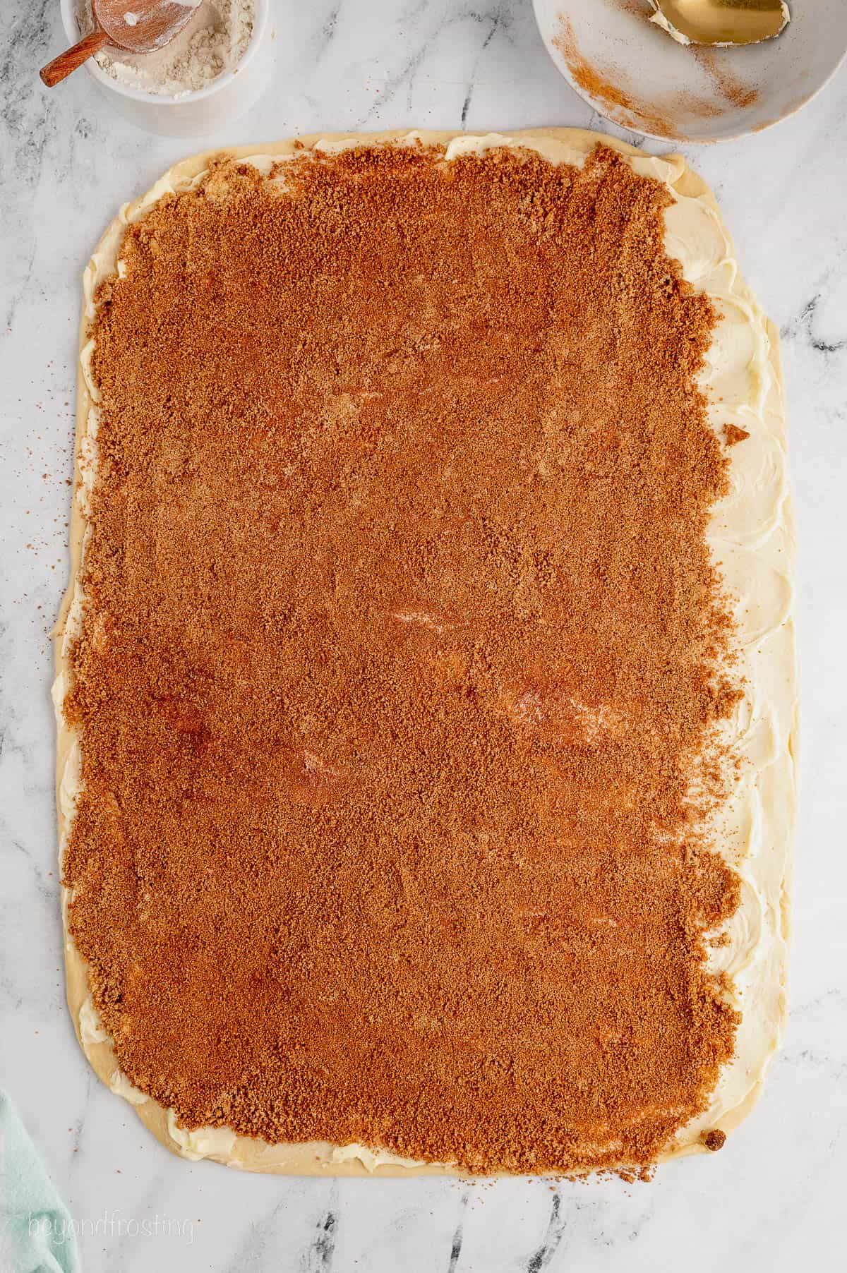 Cinnamon sugar spread over a large buttered dough rectangle.