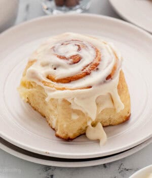 A cinnamon roll topped with cream cheese frosting on a plate.