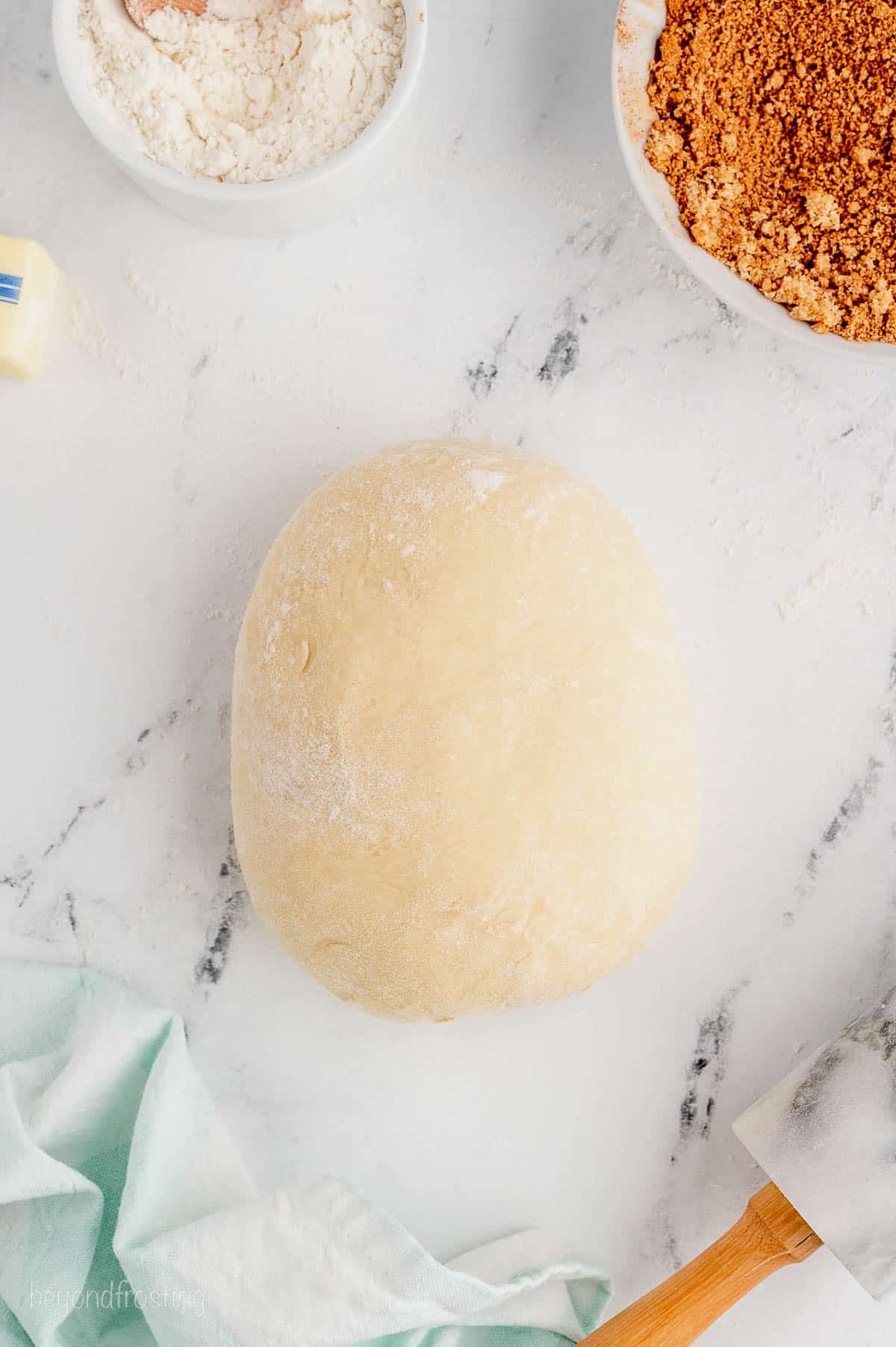 A ball of cinnamon roll dough on a countertop next to a bowl of cinnamon sugar.