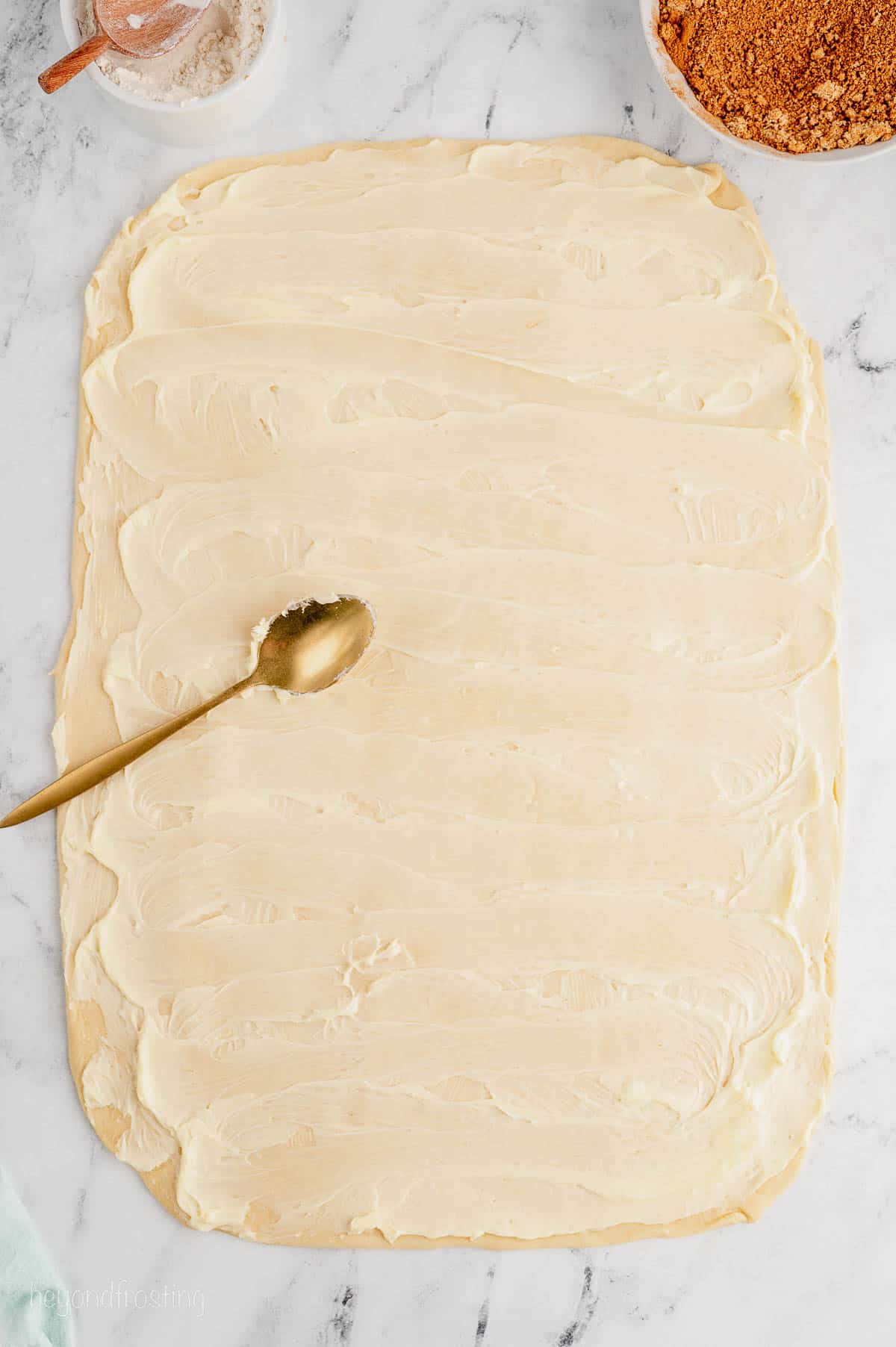 A spoon on top of a large dough rectangle spread with softened butter.