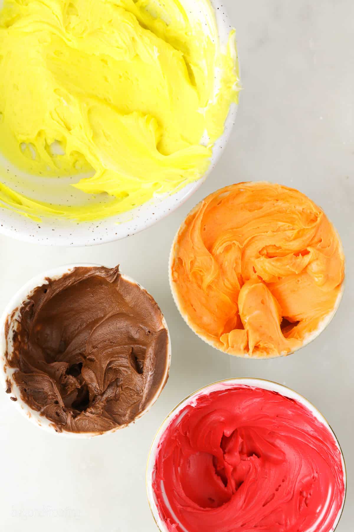 4 bowls with colored buttercream: yellow, brown, orange and red