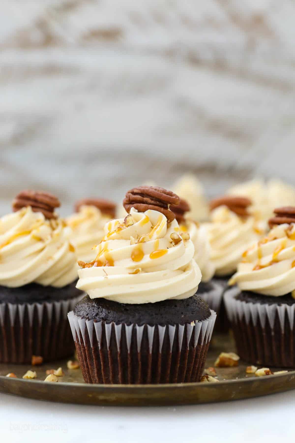 side view of a platter filled with chocolate cupcakes with caramel buttercream.