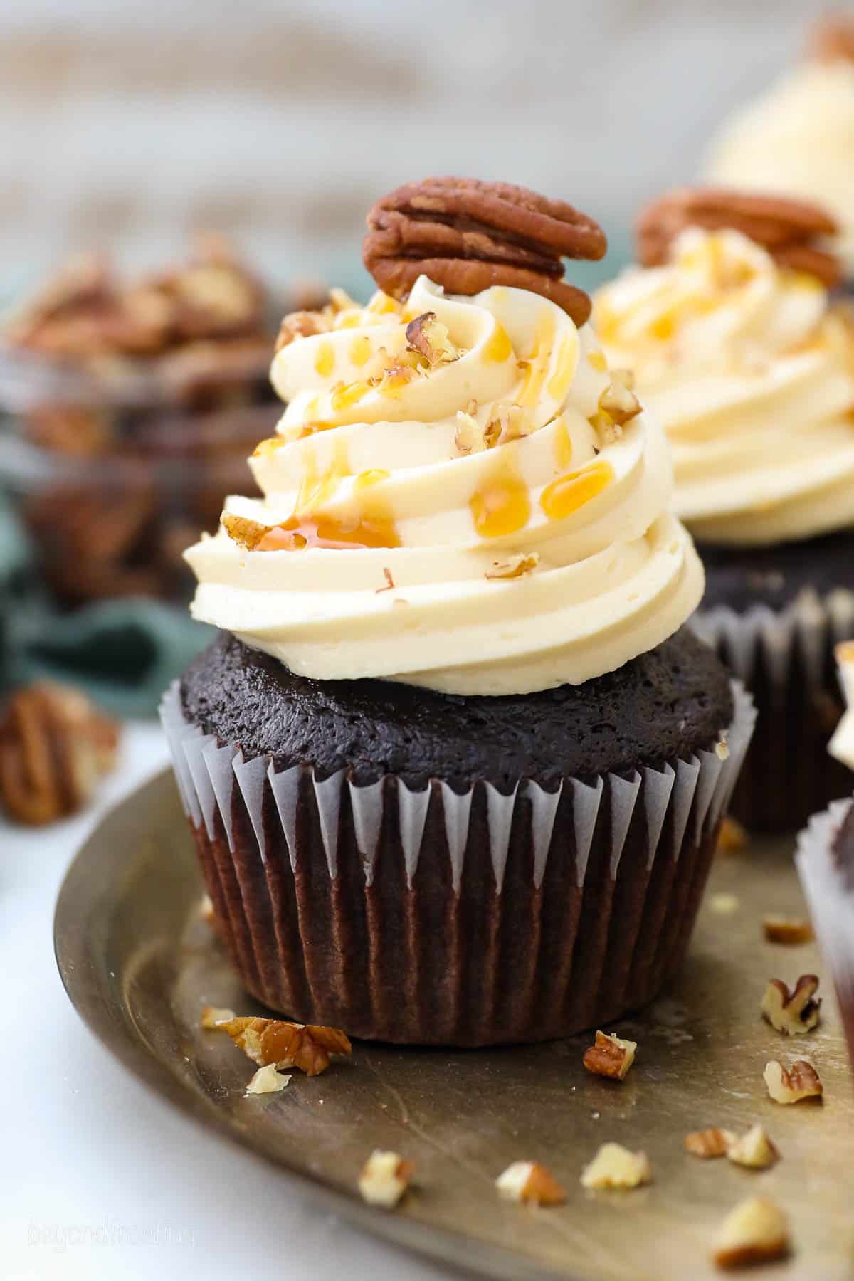 side view of a frosted chocolate cupcake topped with a pecan on a platter.