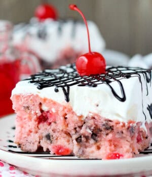 closeup of a slice of cherry poke cake topped with chocolate and a cherry