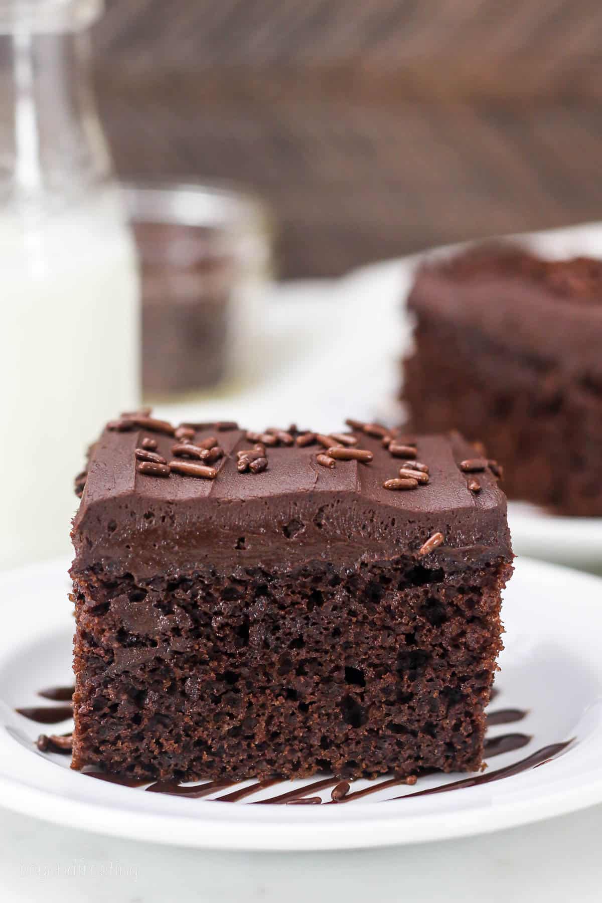side view of a slice of frosted chocolate cake on a plate drizzled with chocolate