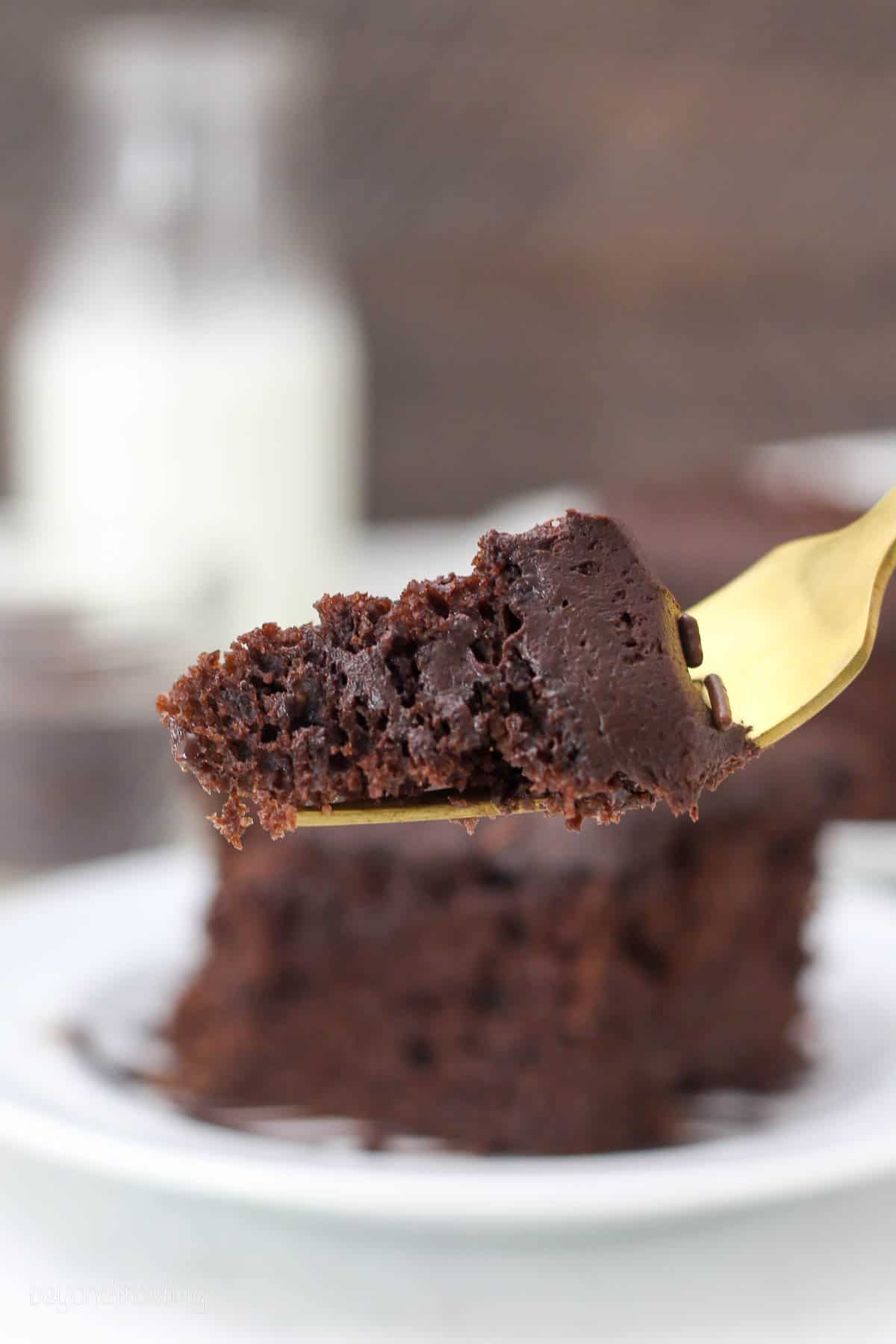 a gold fork held with a bite of chocolate cake