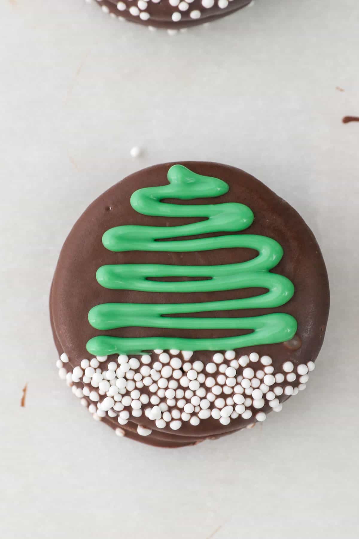 A Christmas Oreo decorated with a piped green Christmas tree and white sprinkles.