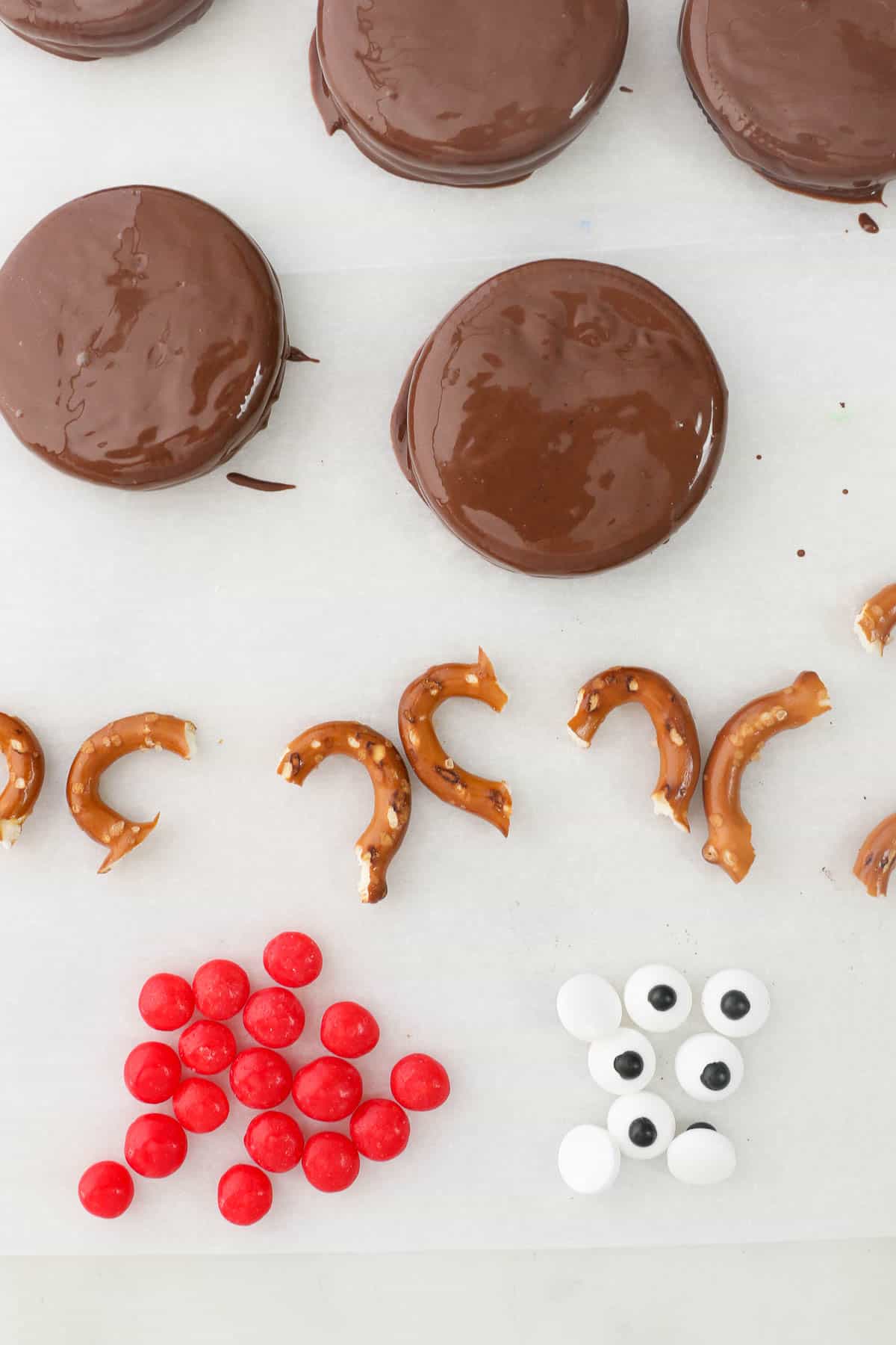 The pretzel antlers, red M&M noses, and candy eyes for Reindeer Christmas Oreos next to chocolate covered Oreos.