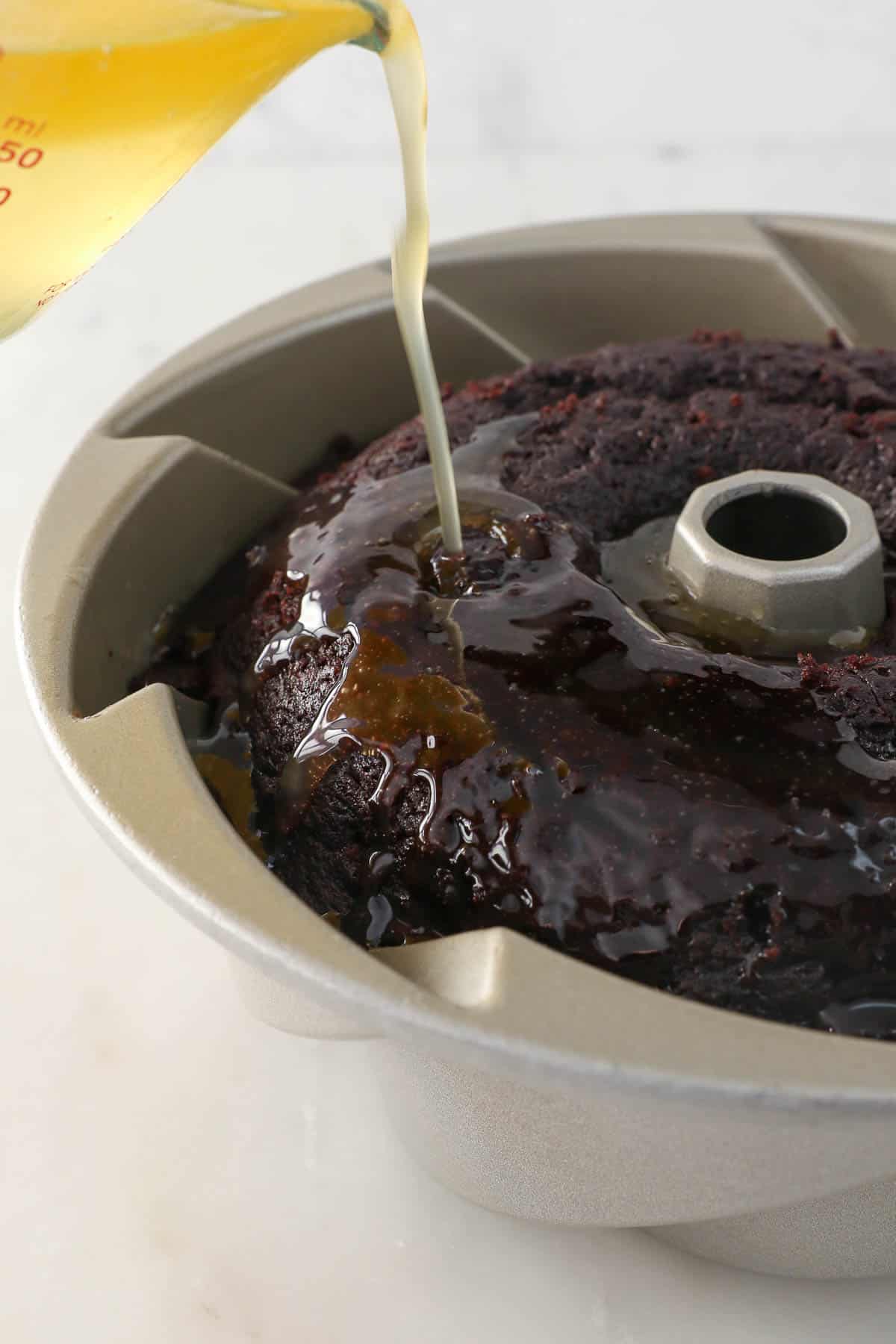 Rum glaze being poured over the top of a chocolate cake in a bundt pan