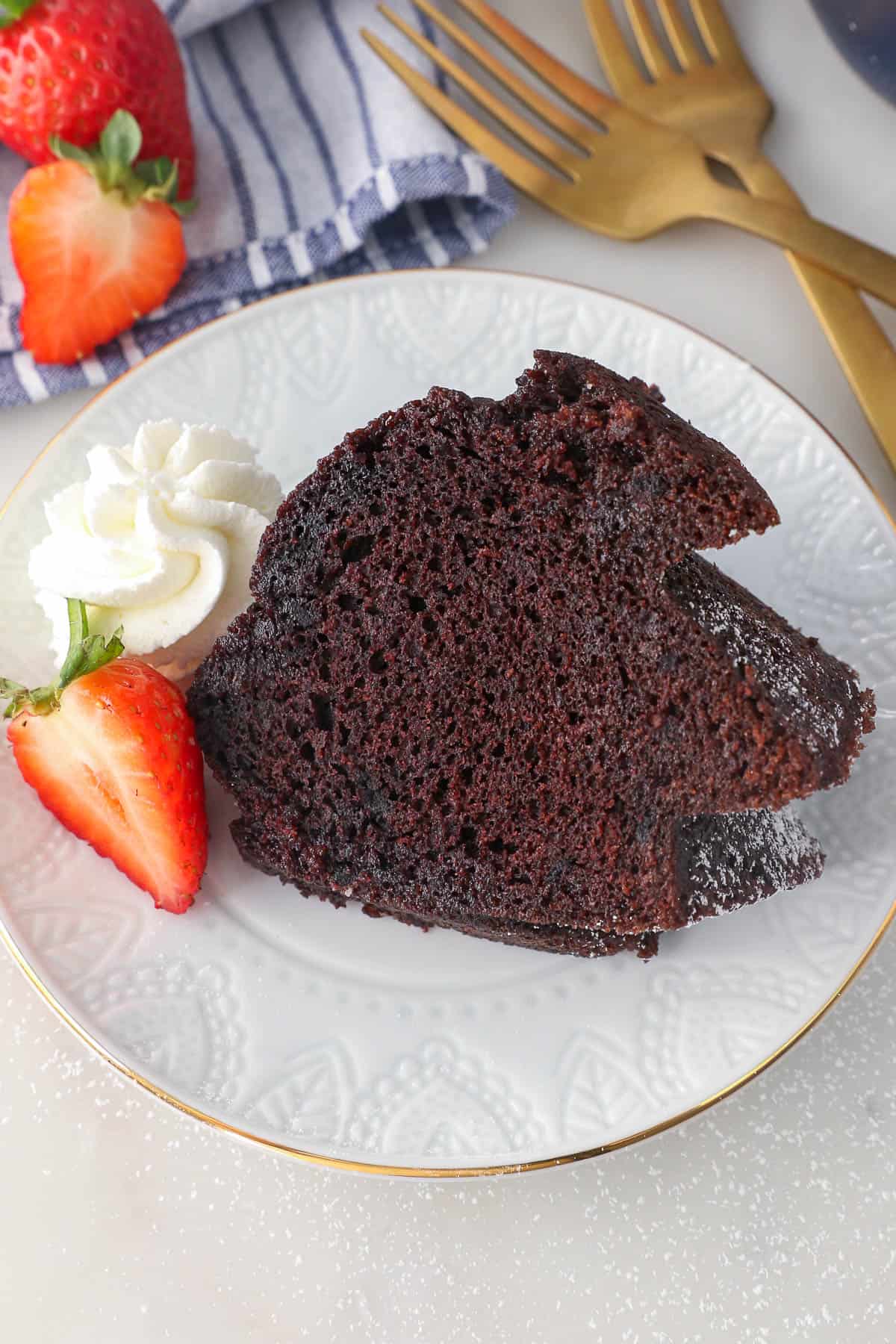 A slice of chocolate rum cake on a plate next to sliced strawberries and a swirl of whipped cream.
