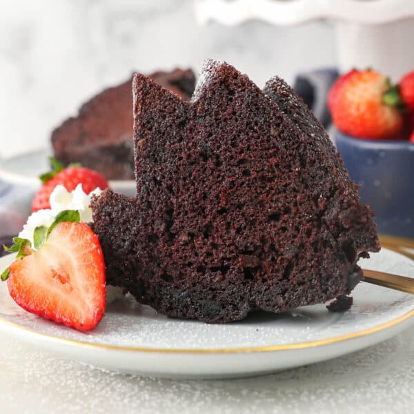 A slice of chocolate rum cake on a plate next to sliced strawberries and a swirl of whipped cream.