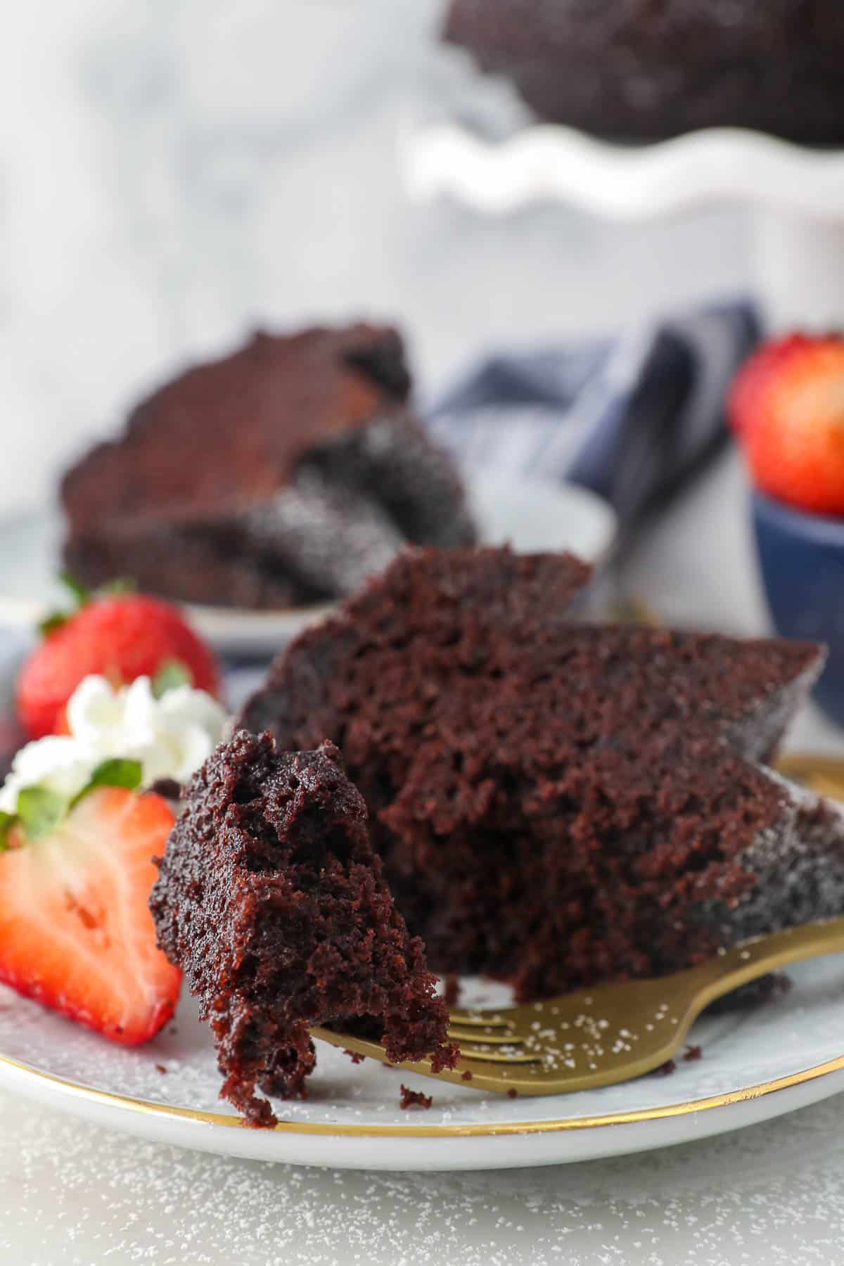 A forkful of chocolate rum cake next to a slice on a plate with strawberries.