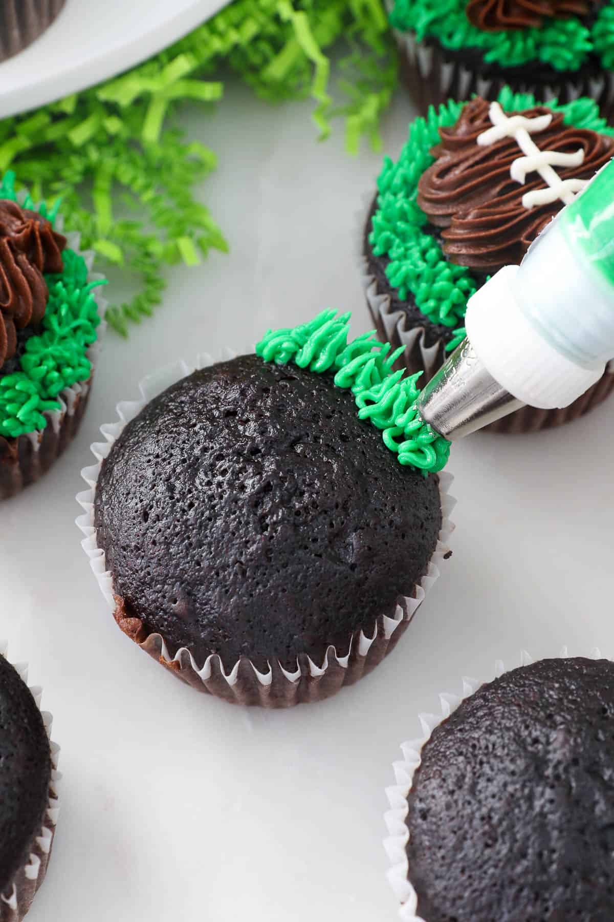 A piping tip pipes green frosting grass around the edges of a chocolate cupcake.