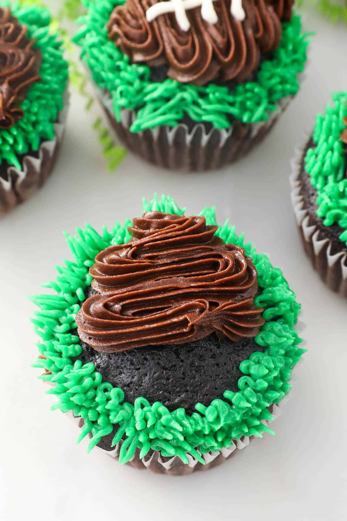 Brown frosting piped over a chocolate cupcake to form the shape of a football, surrounded by green piped frosting grass.