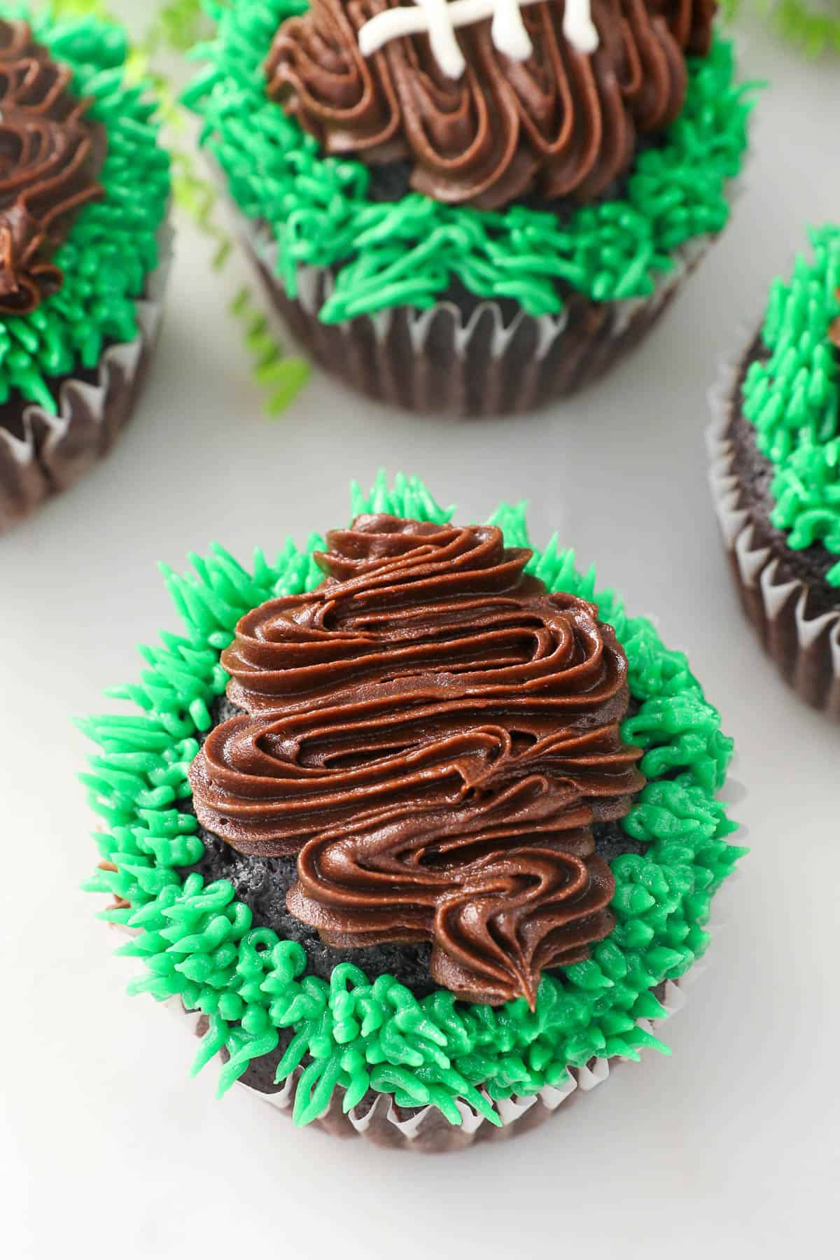 Brown frosting piped over a chocolate cupcake to form the shape of a football, surrounded by green piped frosting grass.