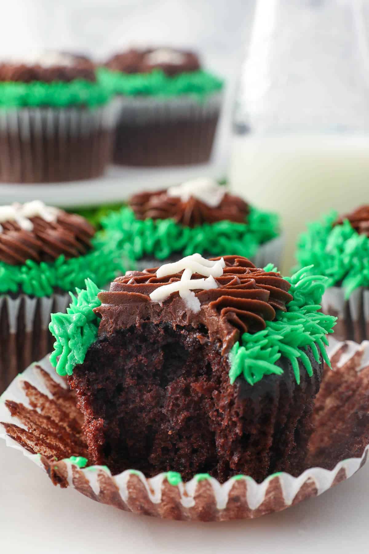 A frosted football cupcake with the cupcake liner peeled away, with a bite missing.